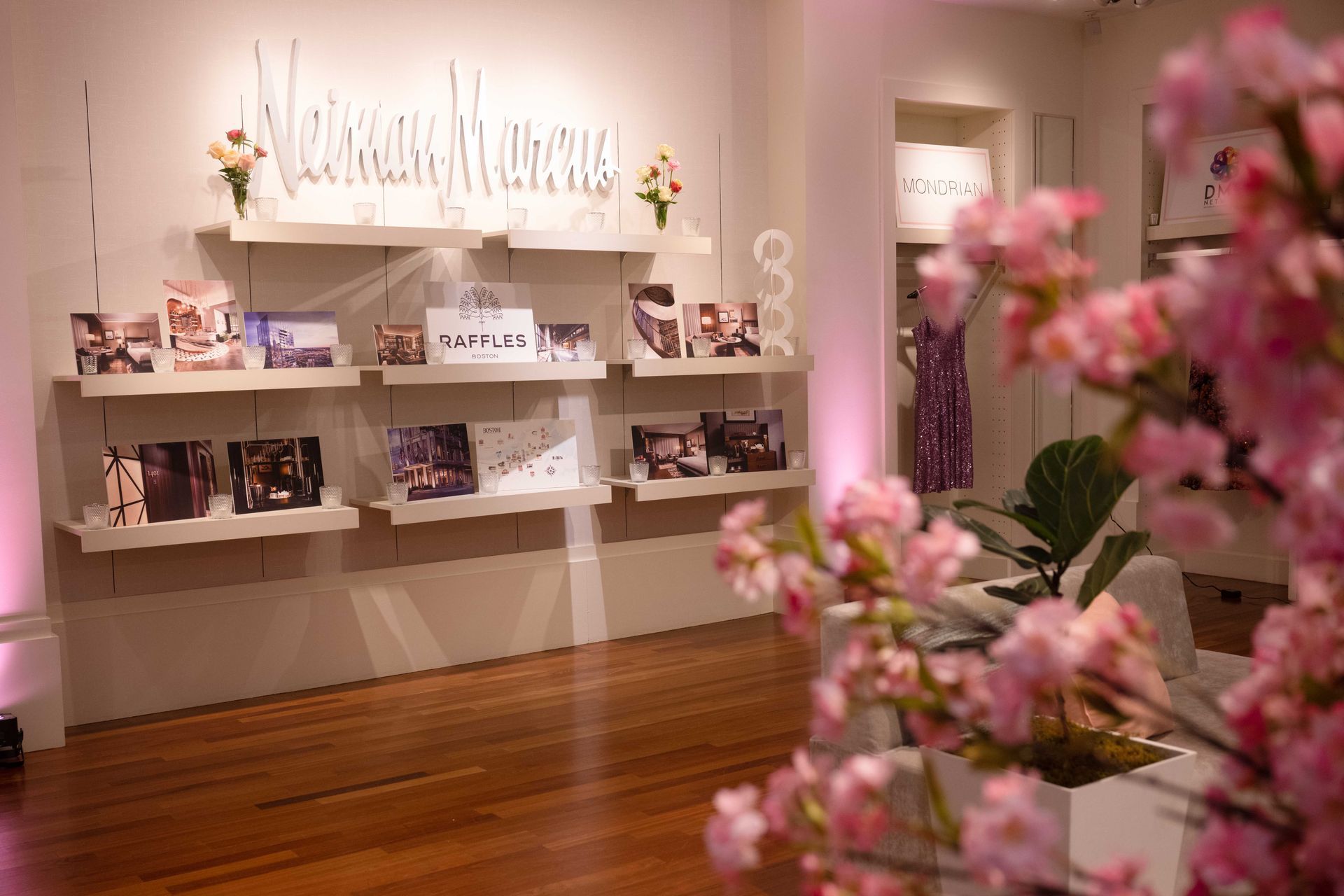 Display shelving with photographs and floral accents. Soft pink lighting and wood flooring.