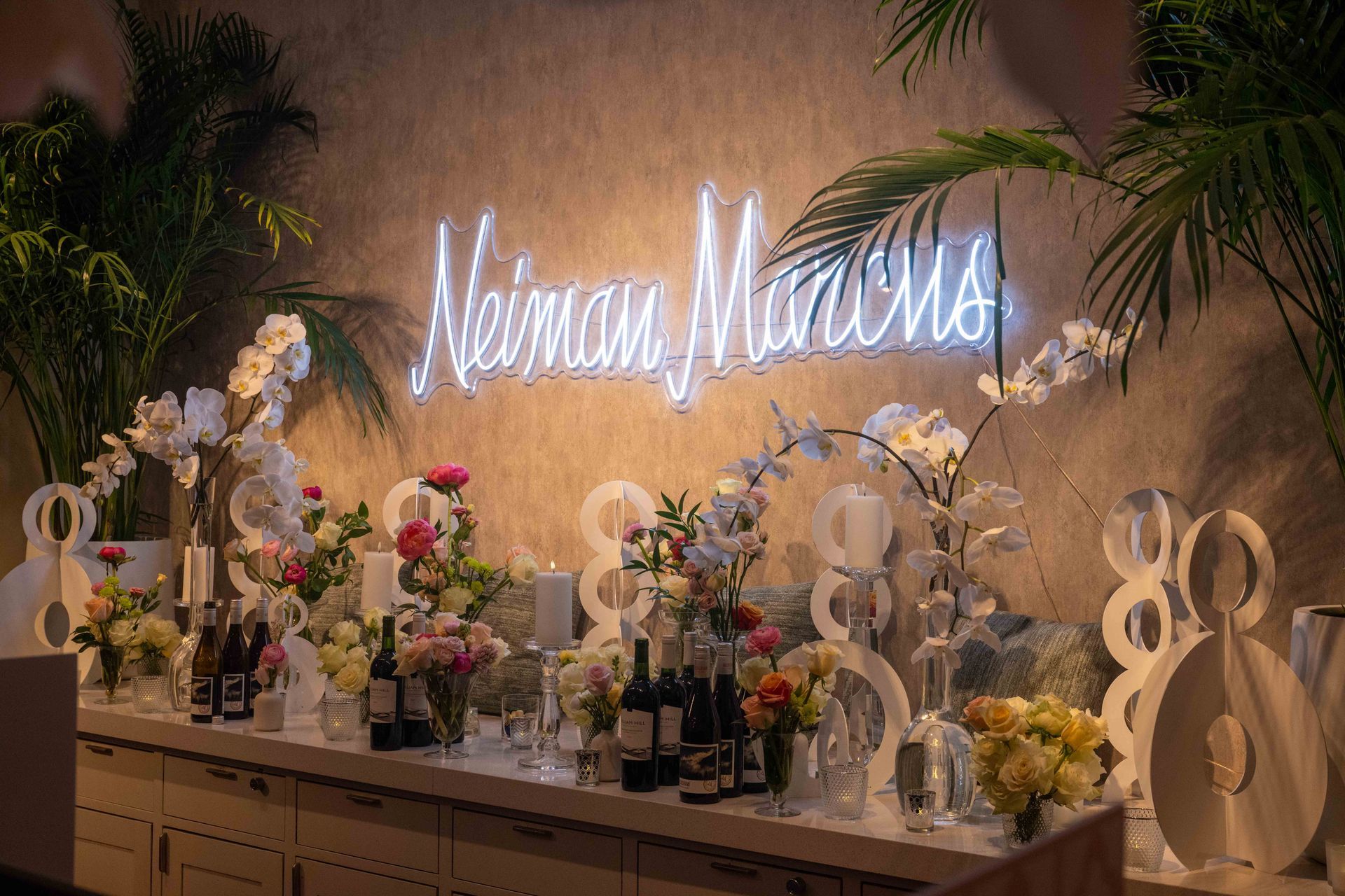 Neiman Marcus bar decorated with flowers, neon sign, and bottles of wine.