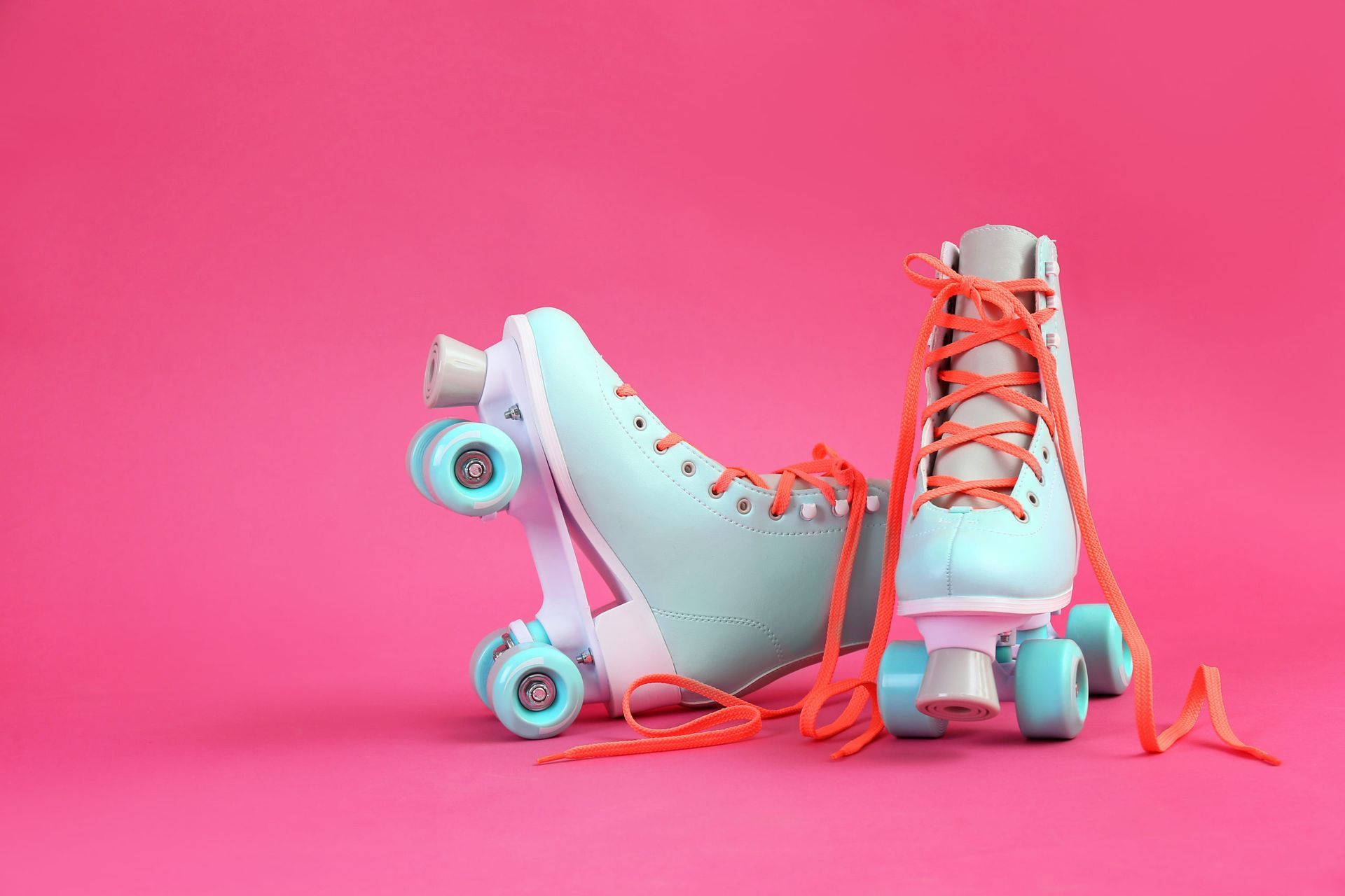 A pair of roller skates with orange laces on a pink background.
