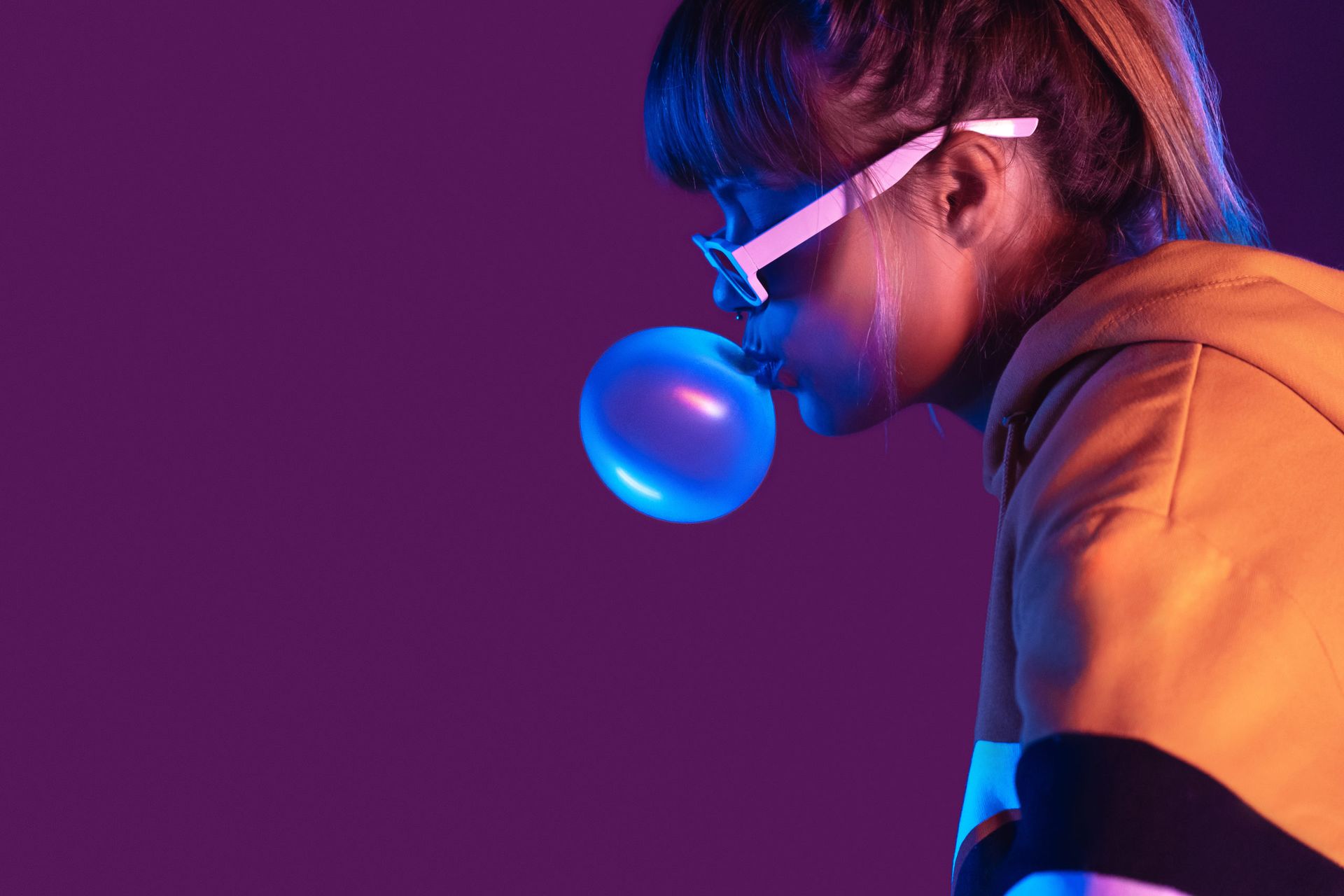 A woman wearing sunglasses is blowing a blue bubble gum.