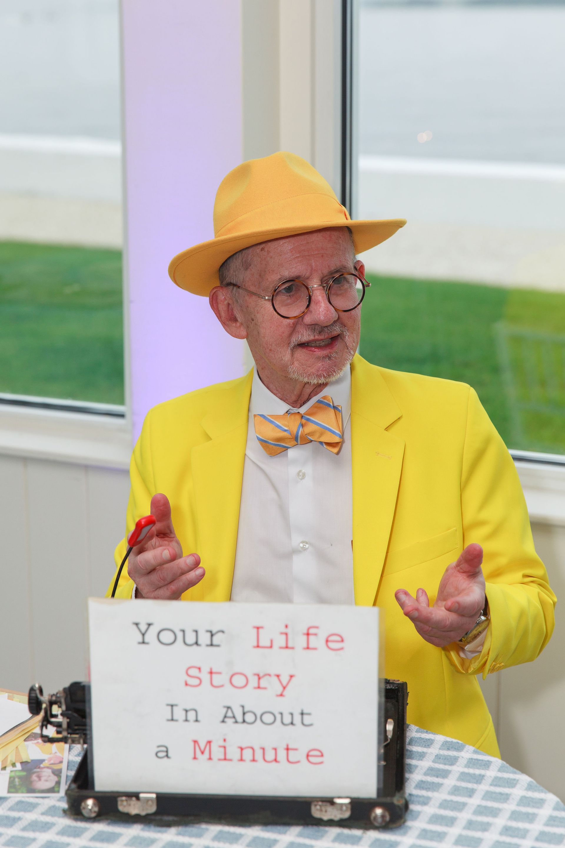 Man in yellow blazer, hat, and bow tie reads 