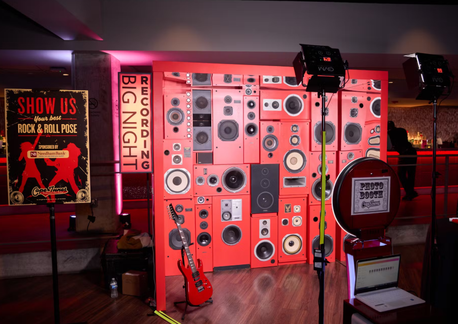 Red wall with speakers, guitar, photo booth, and event sign.
