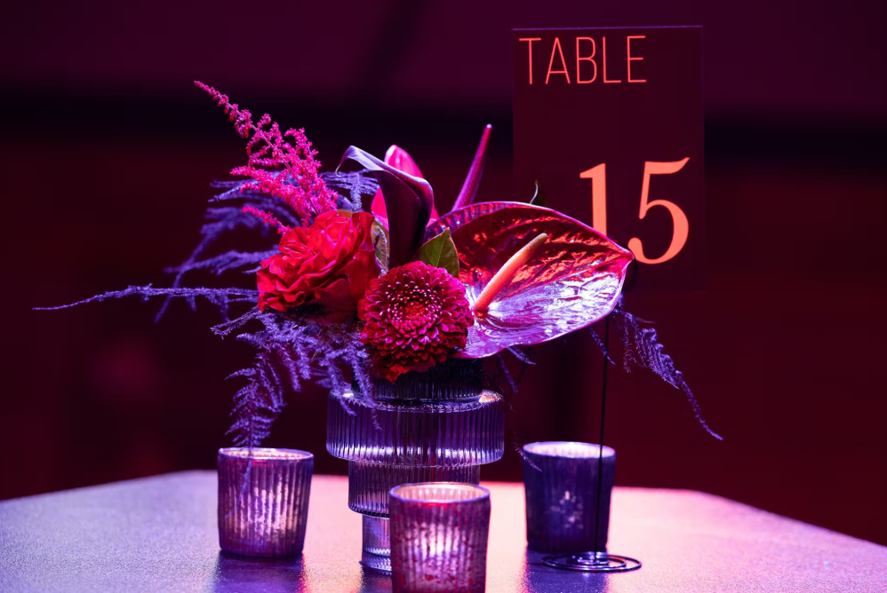 Centerpiece with flowers and table number 15, illuminated in pink and purple light.