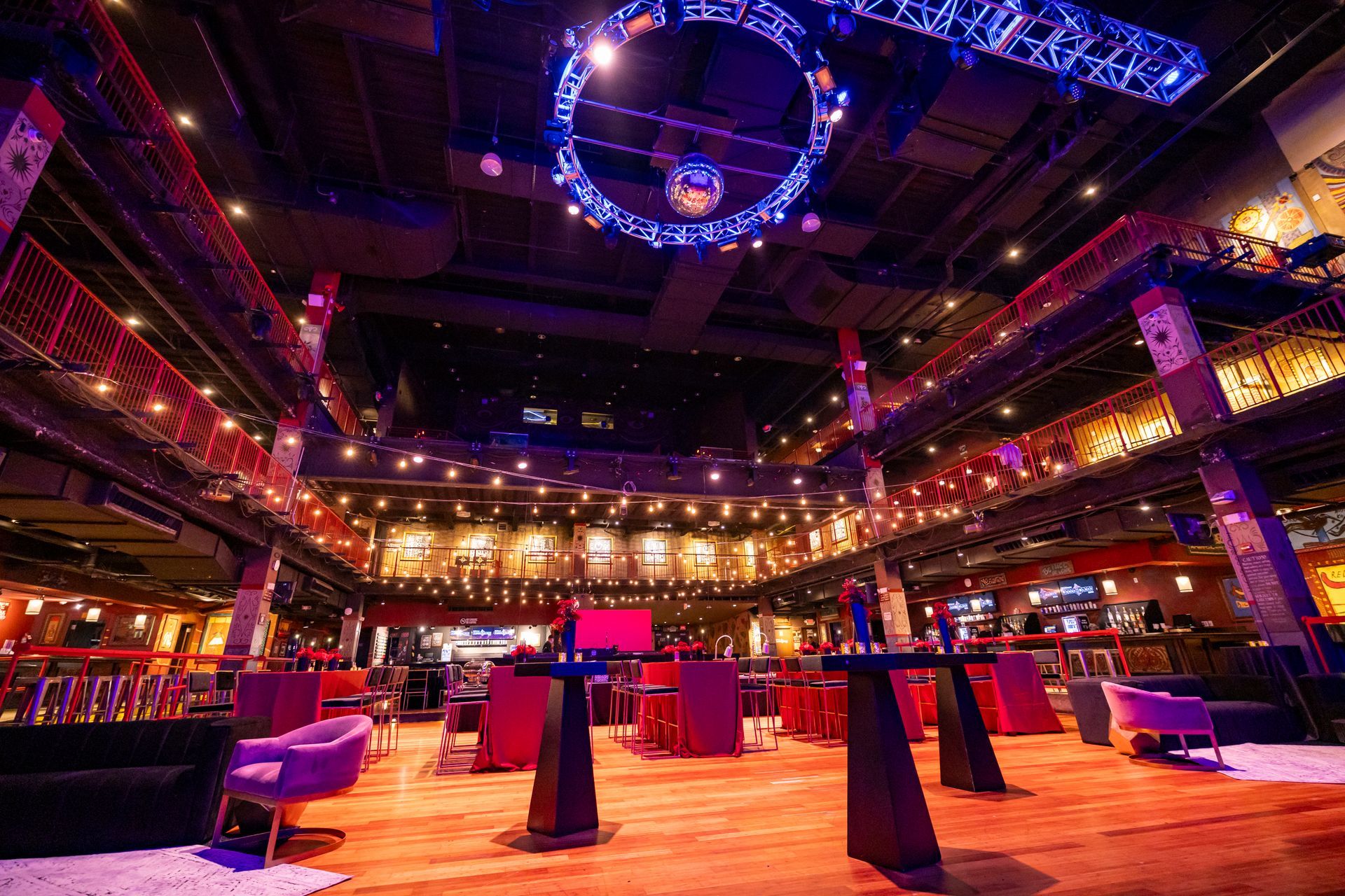 Large, multi-level indoor event space with tables, seating, and stage lighting, with a disco ball.