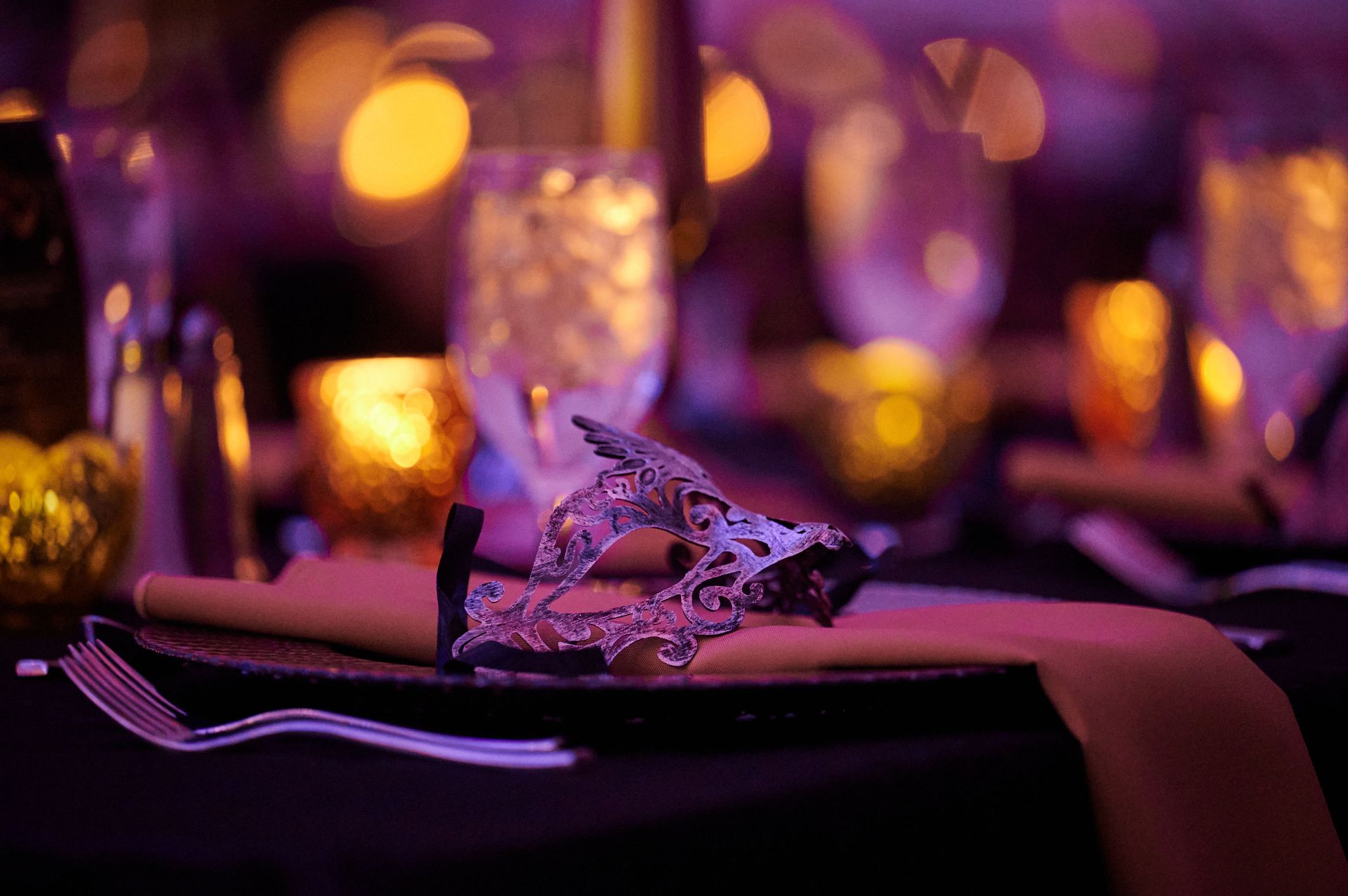 A masked ball table setting: mask on a plate with glasses and candlelight.