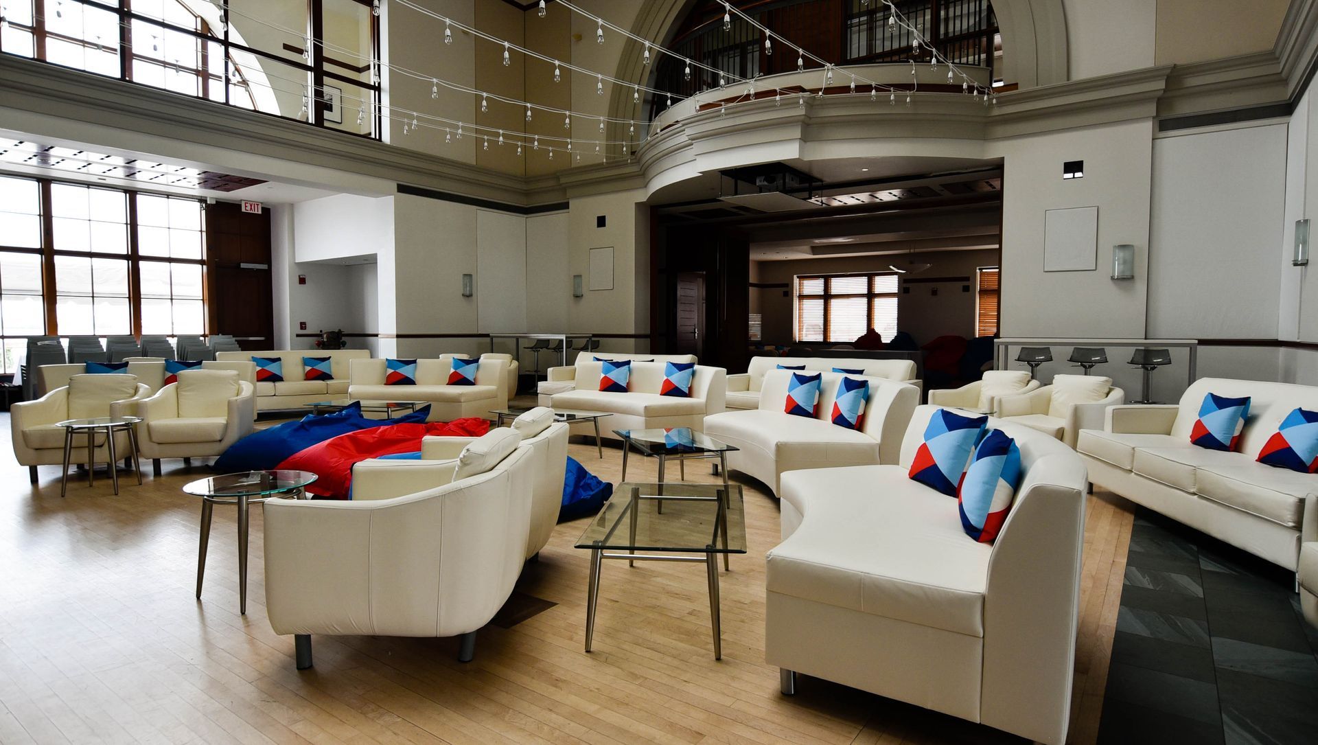 Spacious lounge area with white couches, blue and red pillows, glass tables, and large windows.