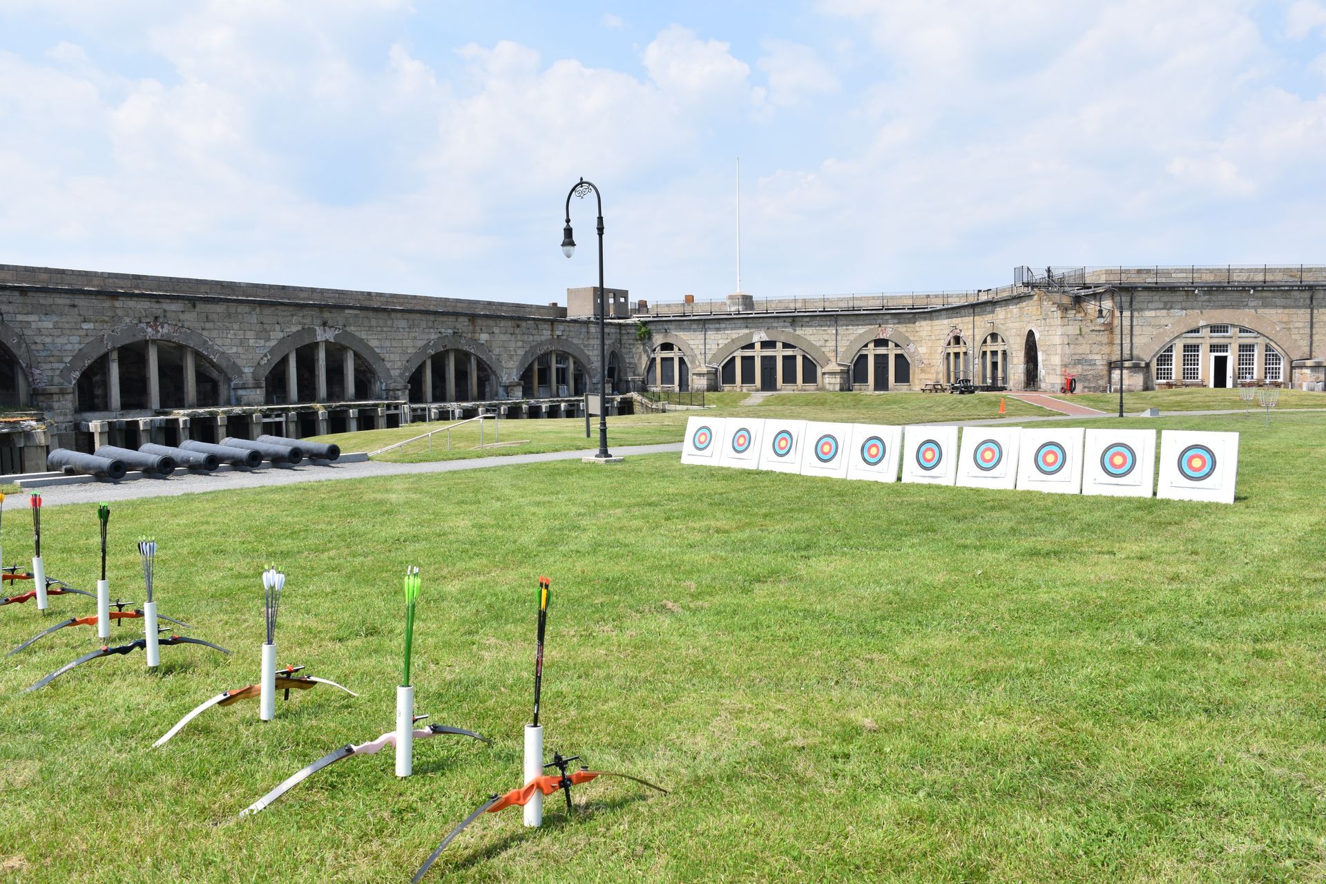 Archery range set up on a grassy field in front of a stone building. Targets, bows, and arrows are visible.