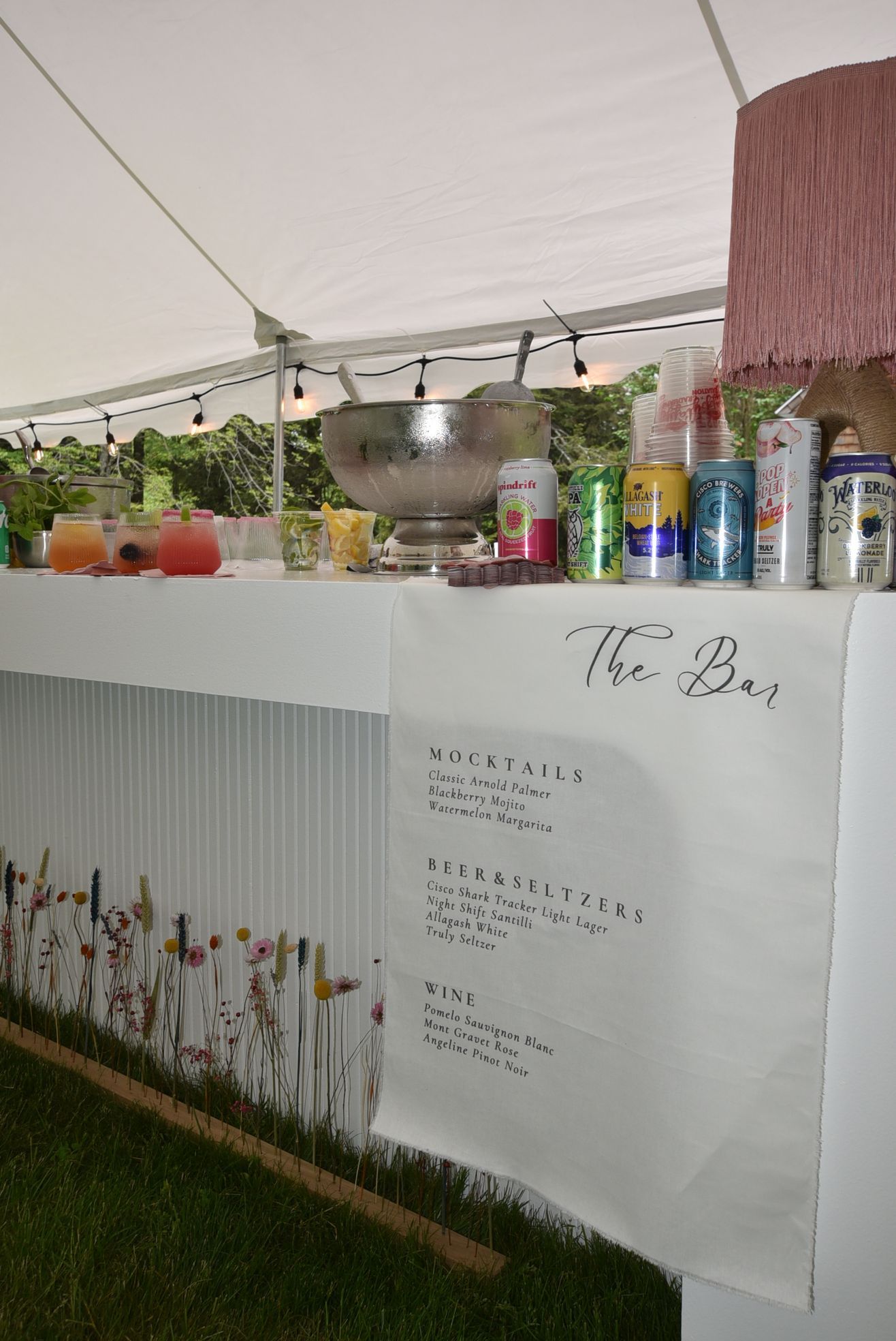 Bar with drinks and menu under a tent, decorated with flowers on the front.