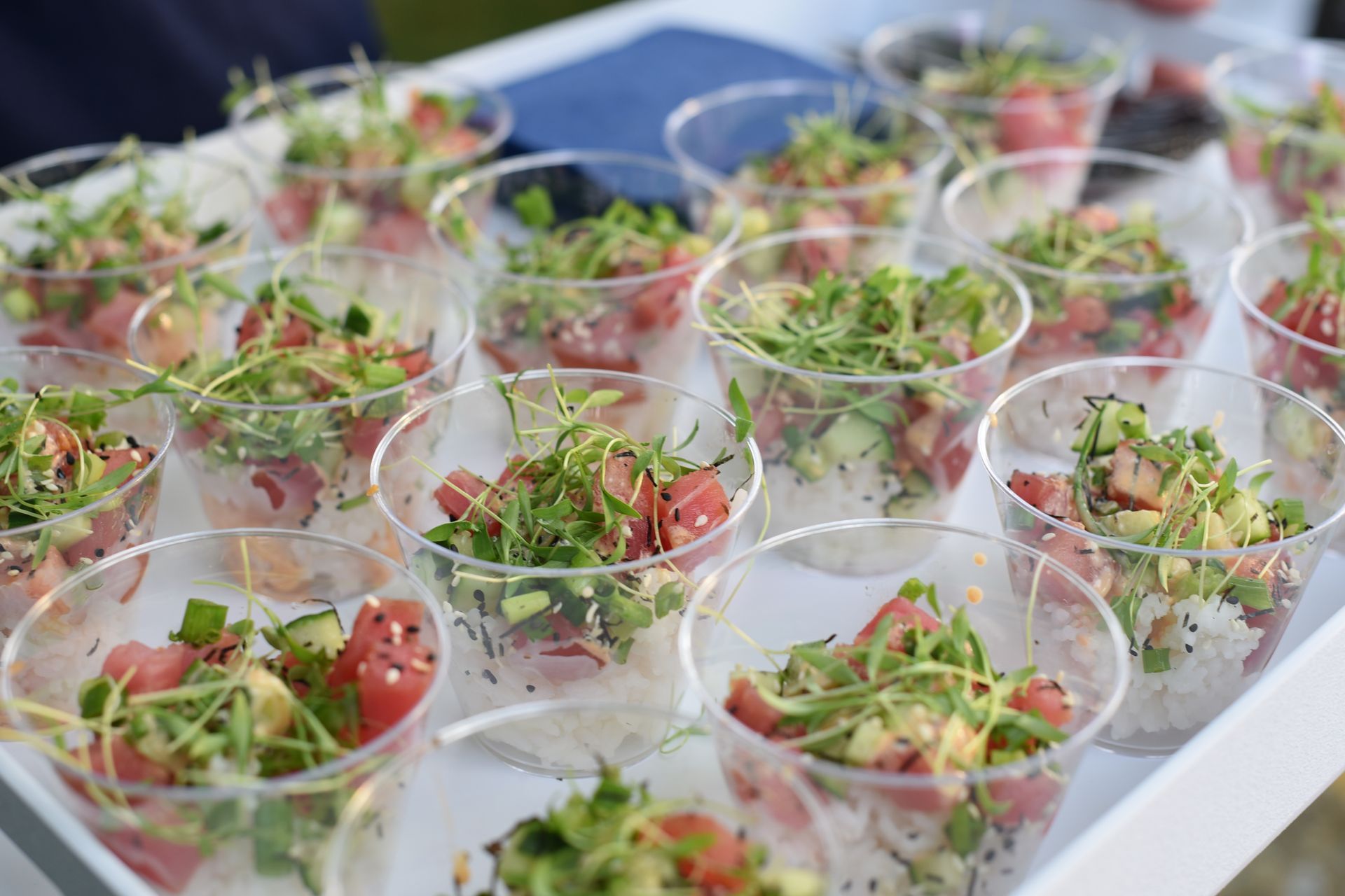 Tray of individual poke bowls in clear cups, containing rice, tuna, avocado, and sprouts.