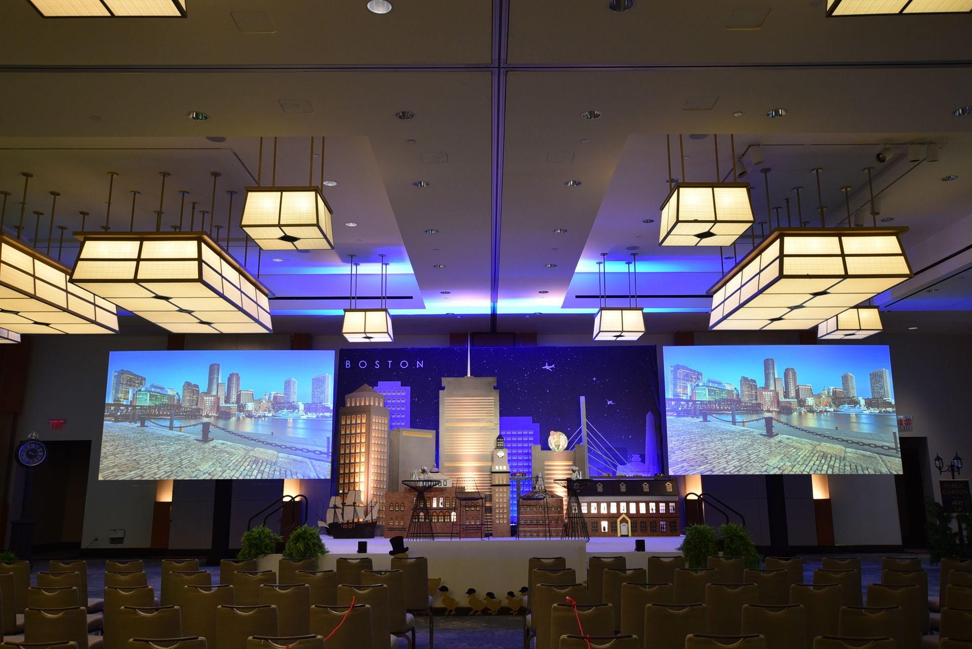 Event stage decorated with a city skyline, screens displaying cityscapes, and hanging square lights.