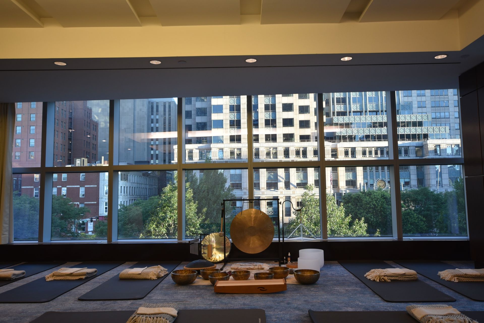 Yoga studio overlooking city buildings; mats, instruments, and a gong in the center.