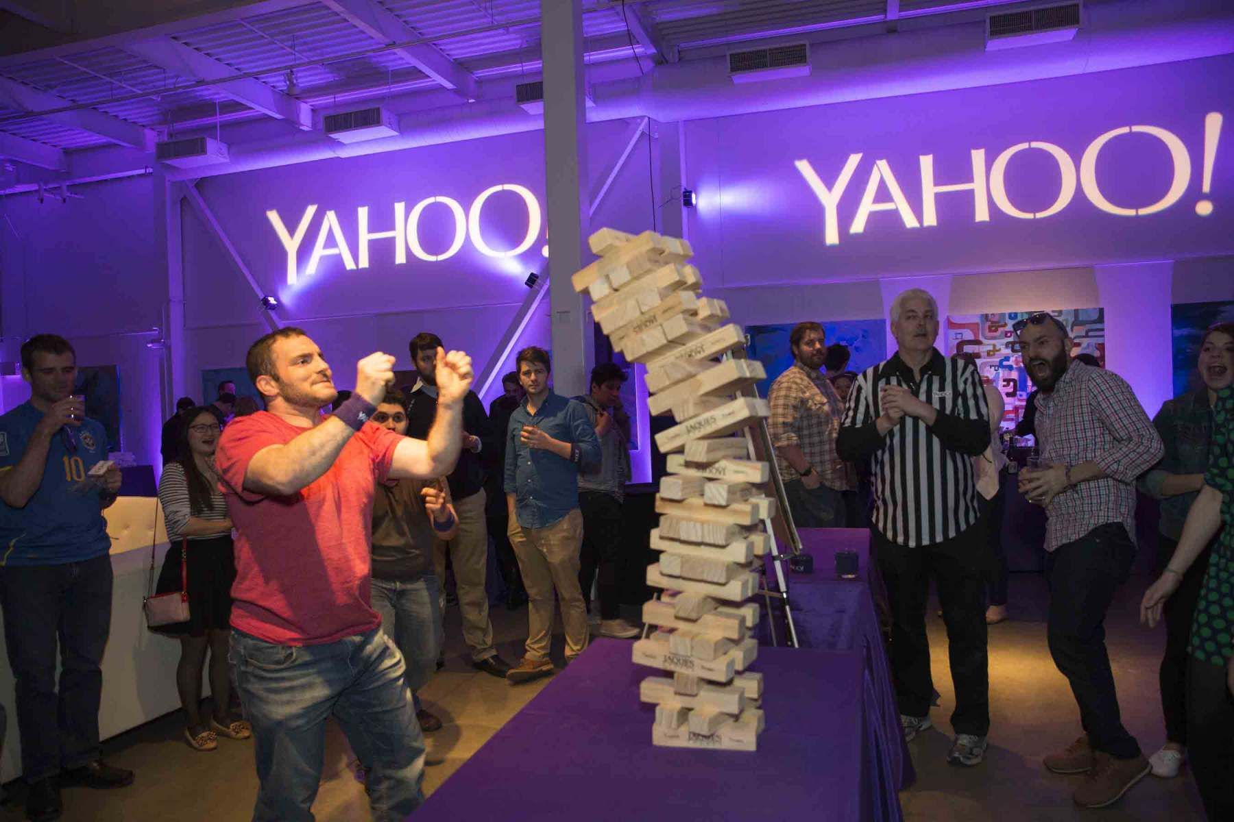 A group of people are playing jenga in front of a yahoo sign.
