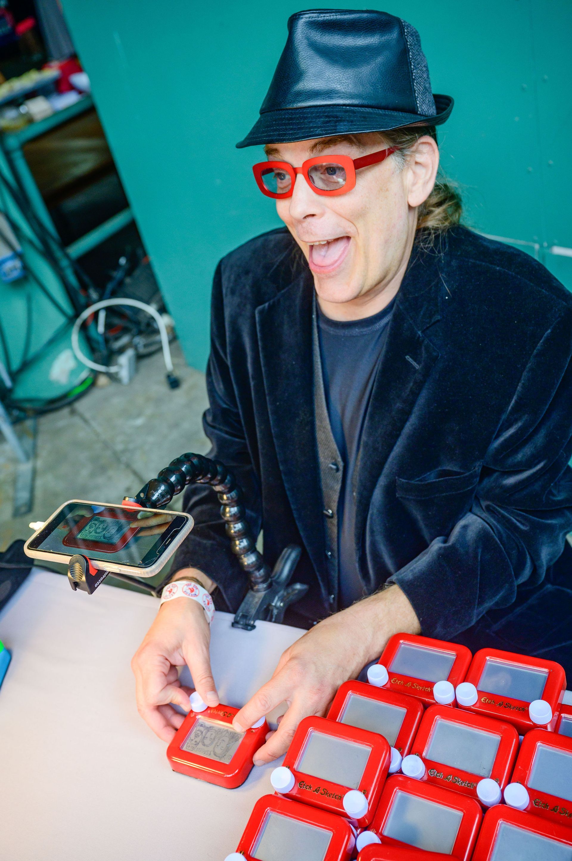Man in black hat and jacket arranging red electronic toys on a table, smiling.