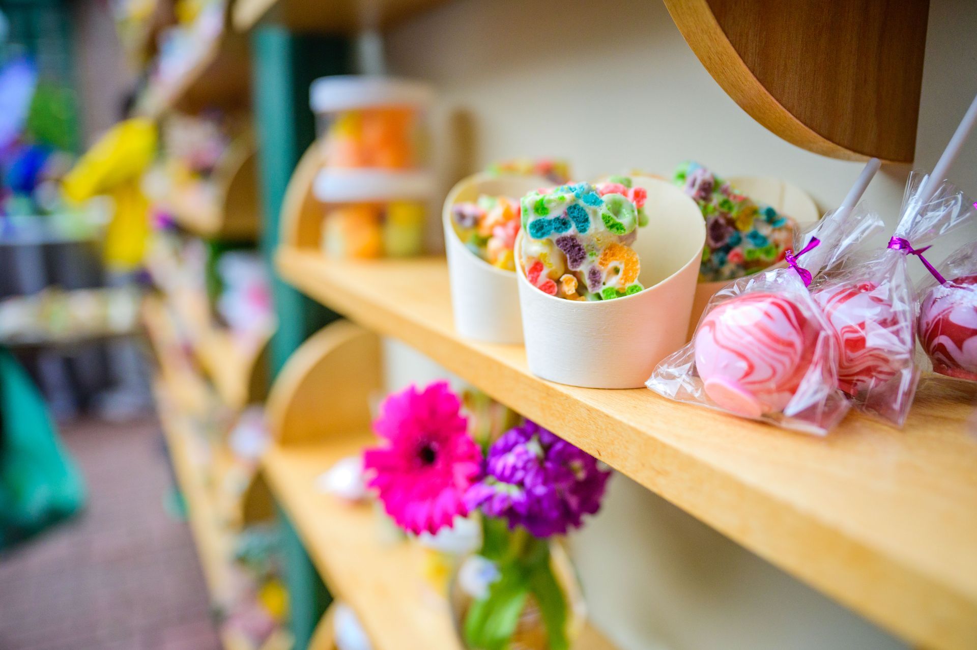 A shelf of colorful treats, including candy-coated popcorn and wrapped sweets, with flowers and wooden accents.