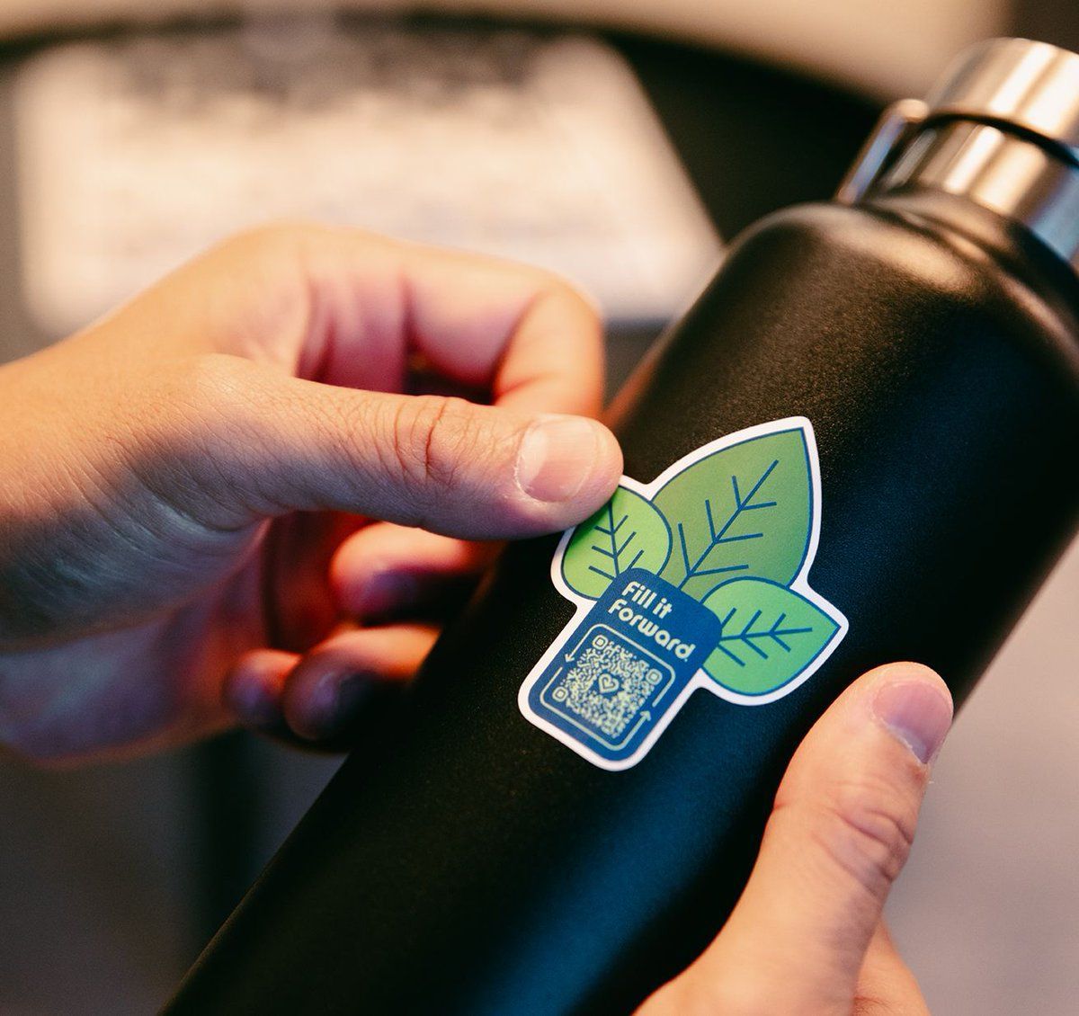 A person holding a clear water bottle with a blue lid and label. The label reads 