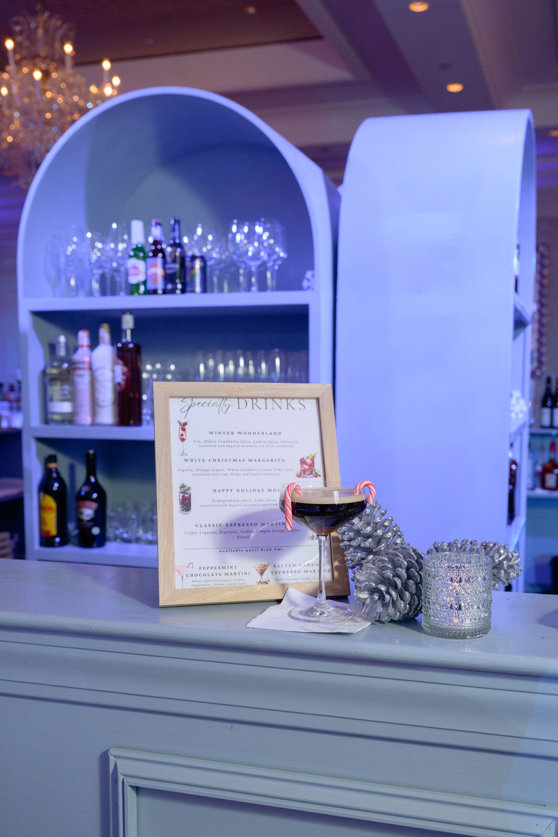 Blue bar with drinks and a menu; string lights on shelves, a cocktail, and a candle holder.