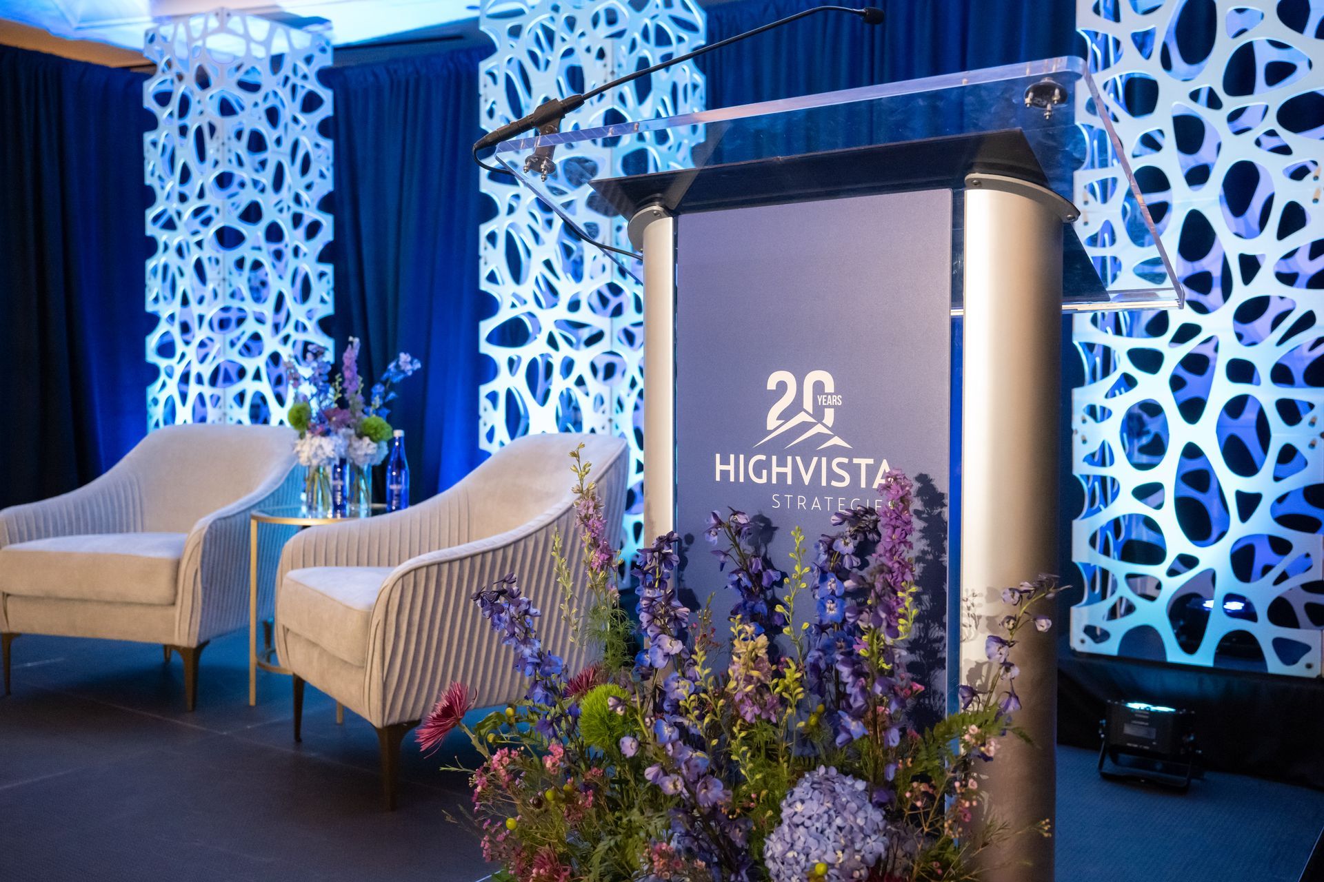 Event podium with floral arrangement and blue-lit decor, featuring a “20 HighVista” sign