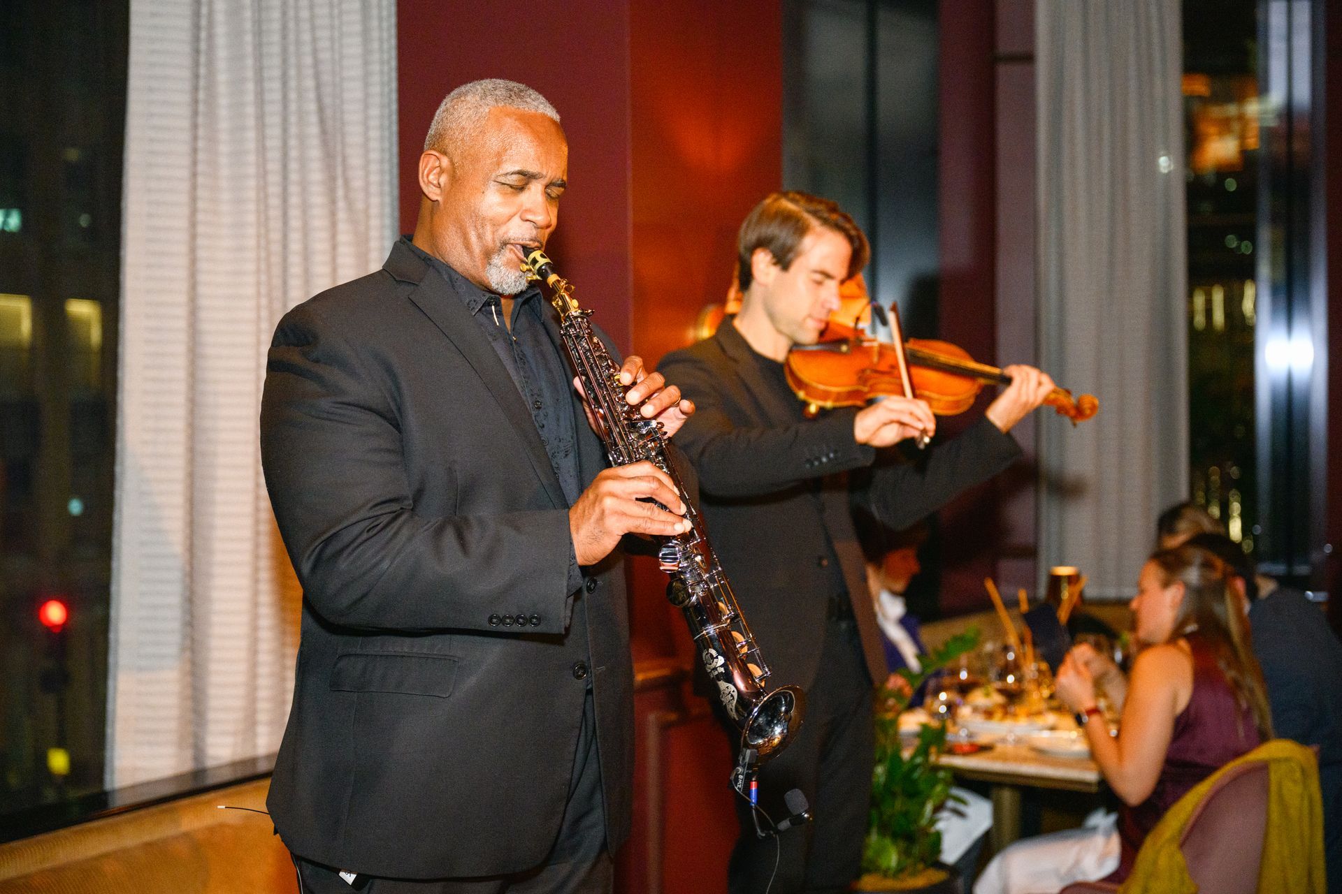 Two musicians performing in a warmly lit restaurant, one playing clarinet and one violin.