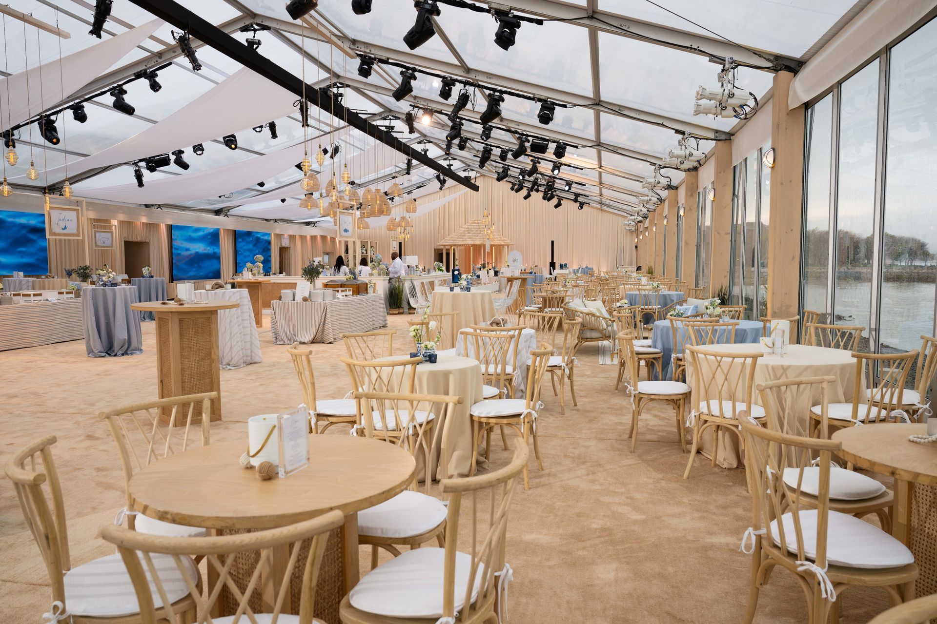 Light wood tables and chairs in a bright tent; ocean views, dining setting.