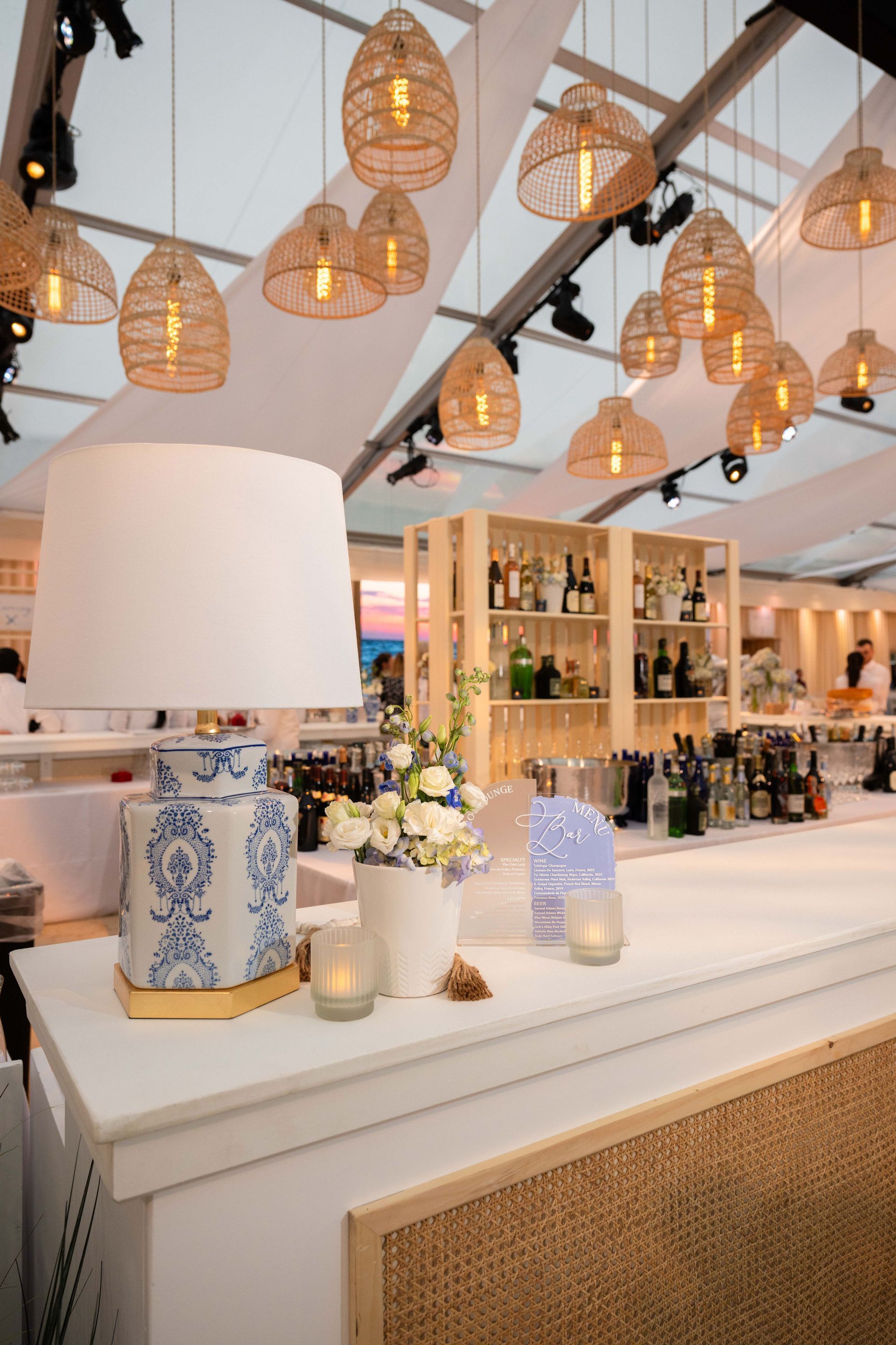 Bar with woven pendant lights, white countertop, blue and white vase, floral arrangement.
