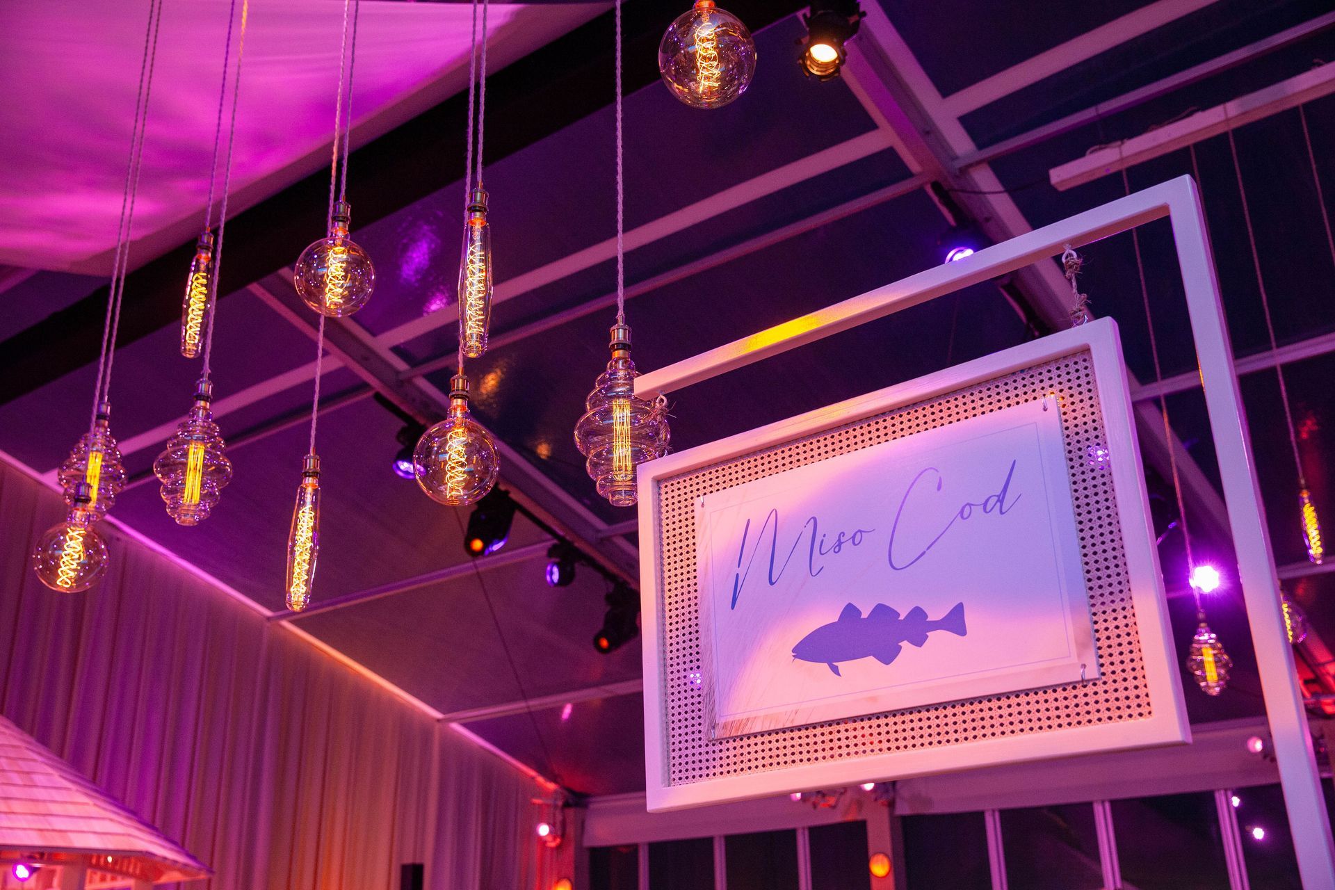 Pink-lit event with hanging Edison bulbs. A sign reads 