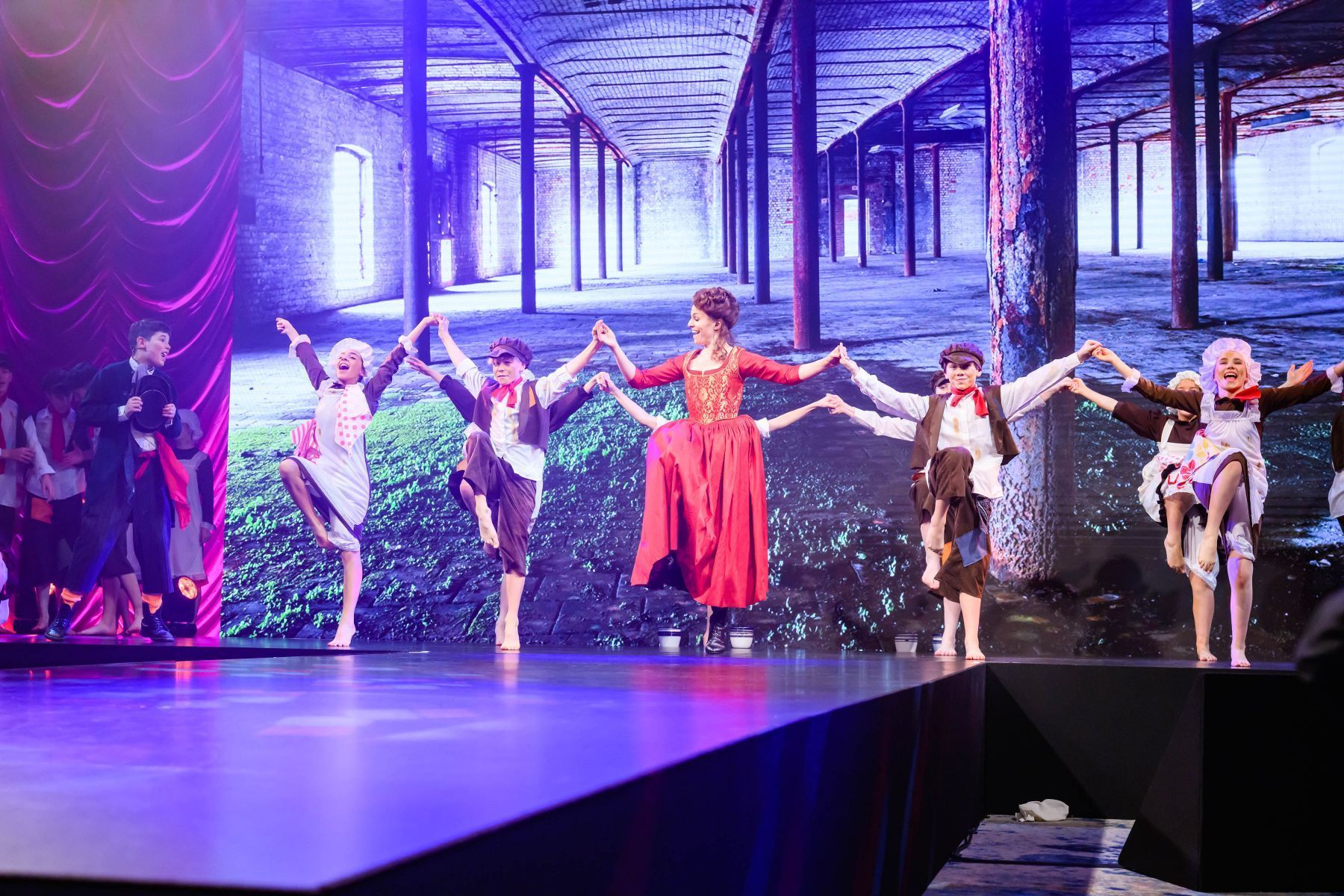 A group of people are dancing on a stage holding hands.