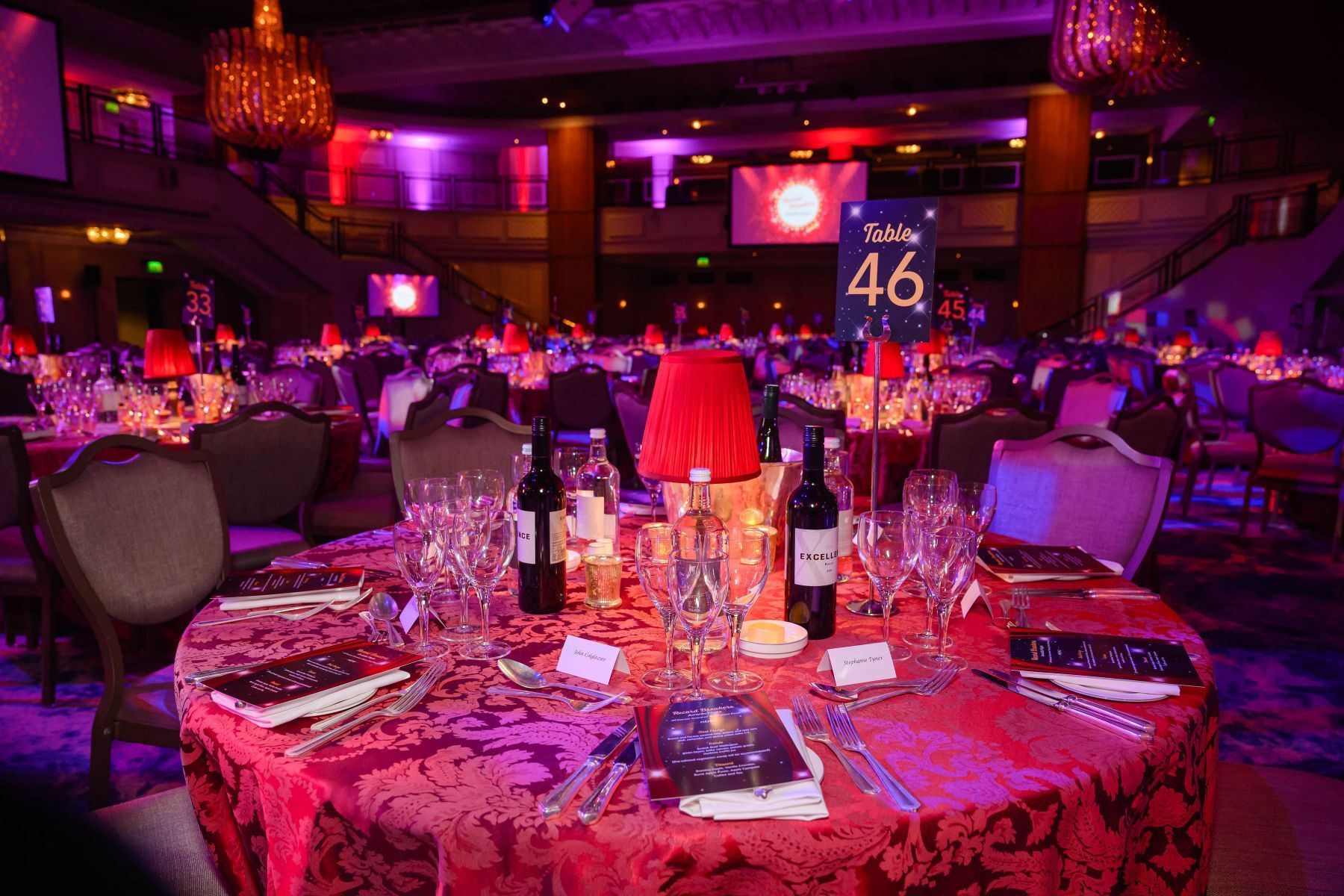 A table set for a dinner party in a large room with purple lights.