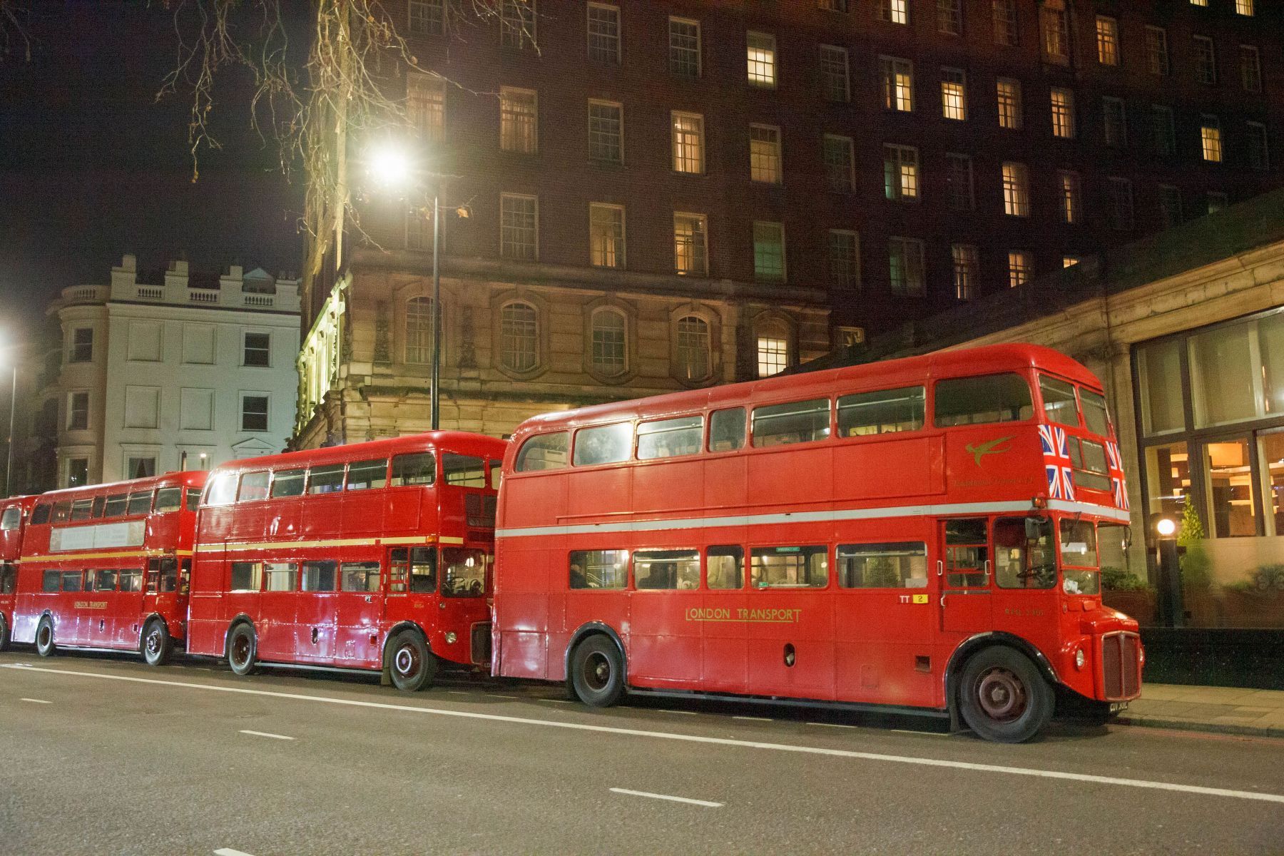 A row of red double decker buses parked on the side of the road