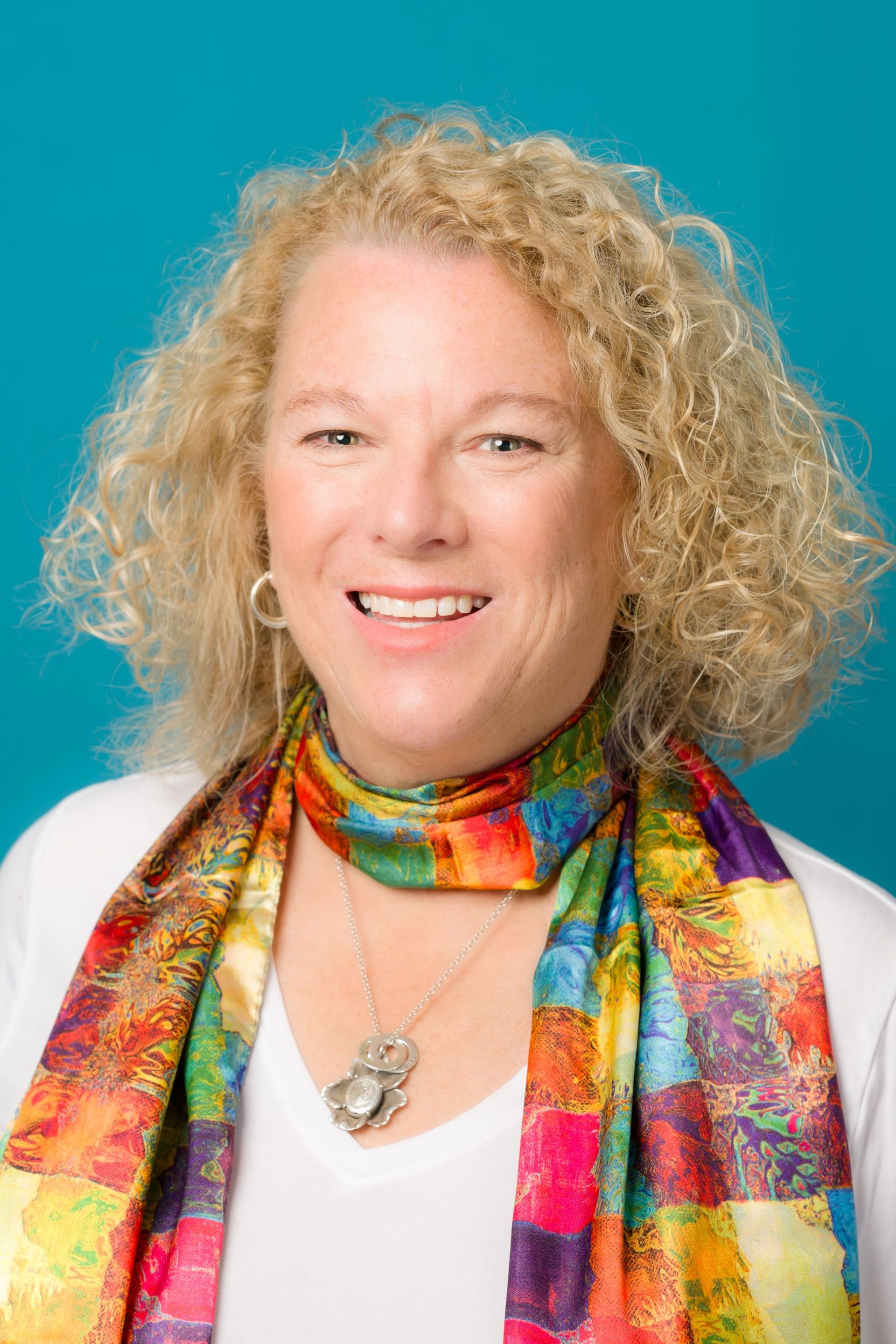 A woman wearing a colorful scarf and a white shirt is smiling.