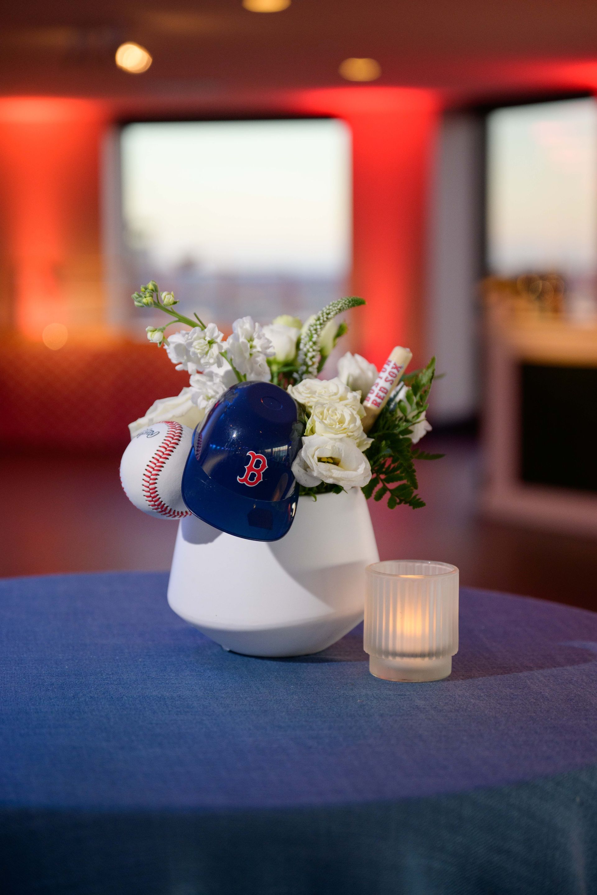 Baseball-themed centerpiece with white flowers, baseballs, and a blue helmet on a blue tablecloth.