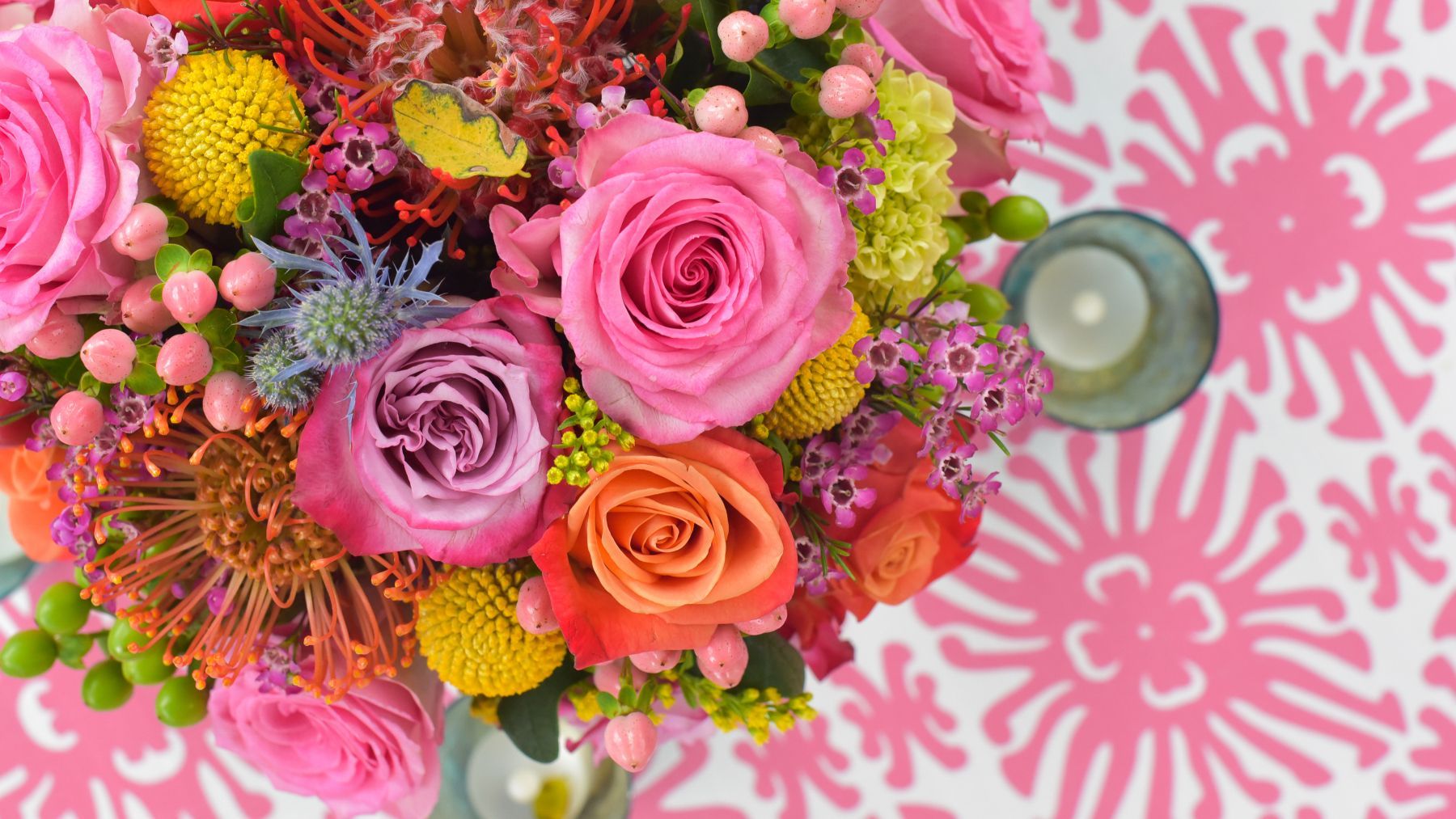 A close up of a bouquet of flowers on a table with a candle.