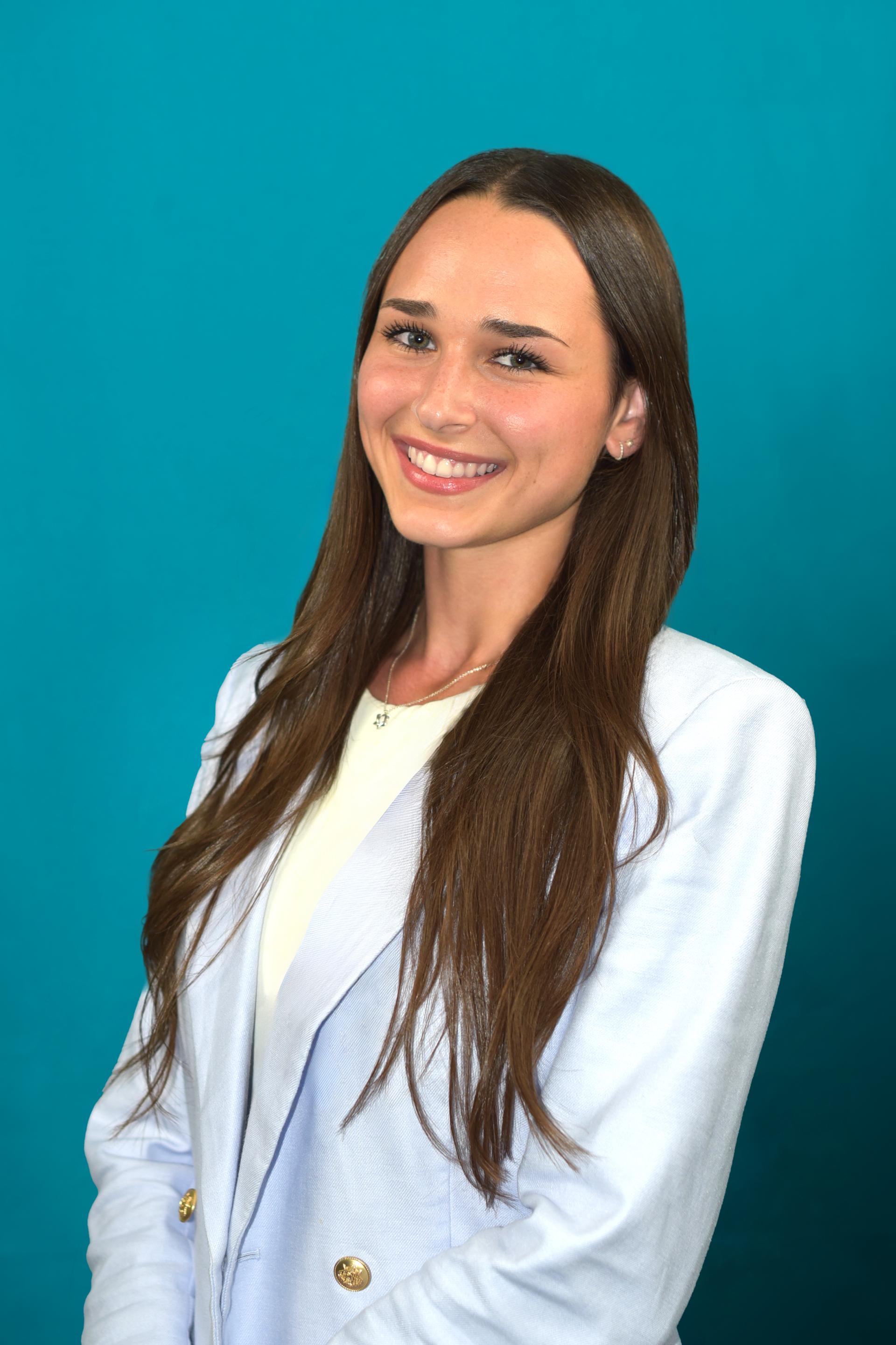 Young woman with long brown hair, wearing a light blue blazer, smiling against a teal background.