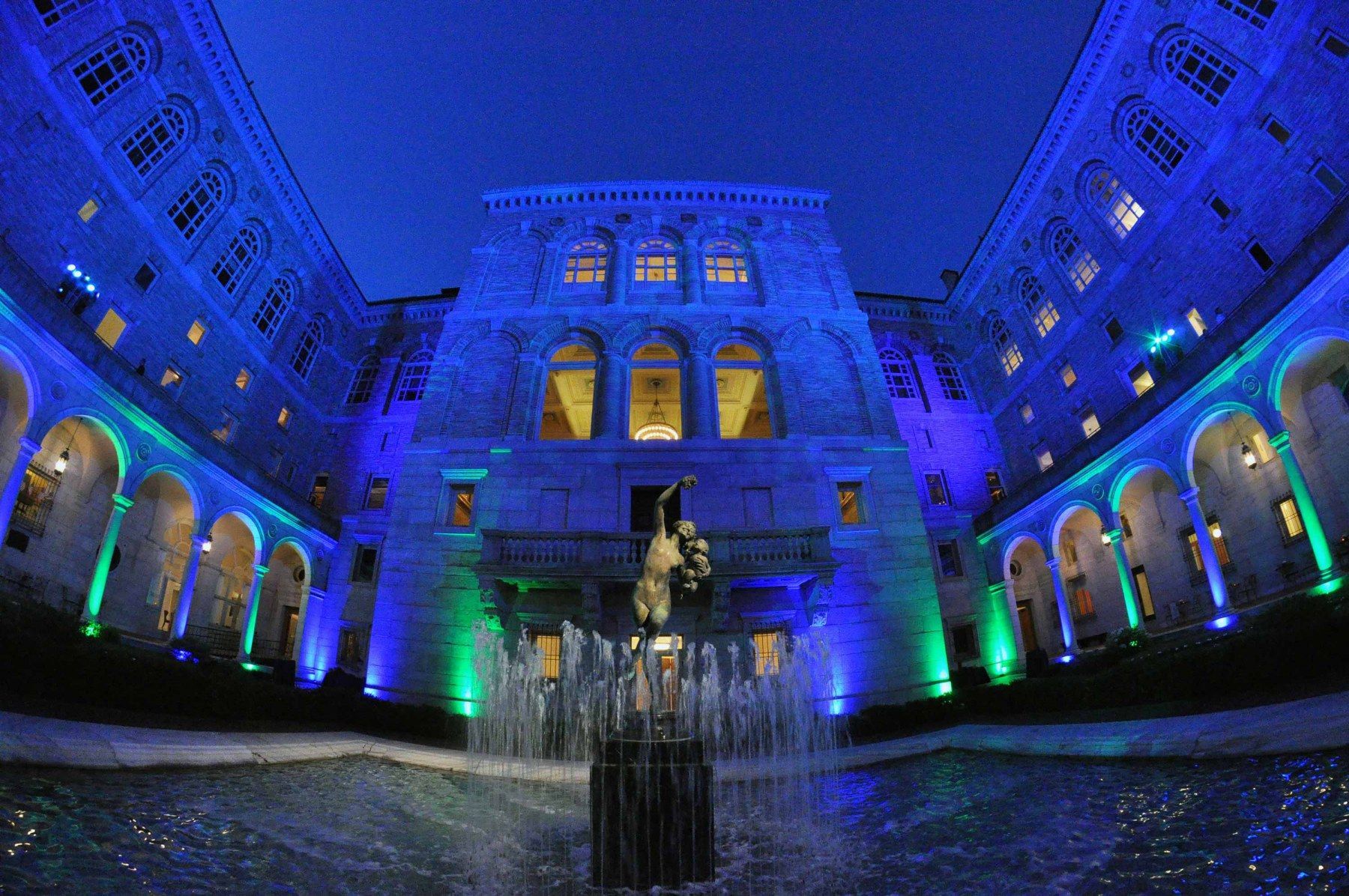 A large building with a fountain in front of it is lit up with blue and green lights.