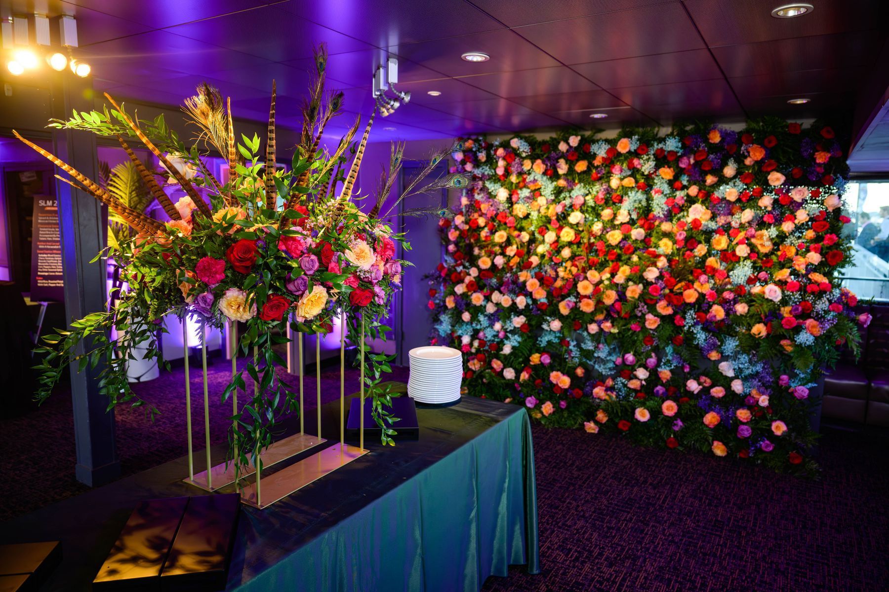 A room with a wall of flowers and a table with flowers on it.