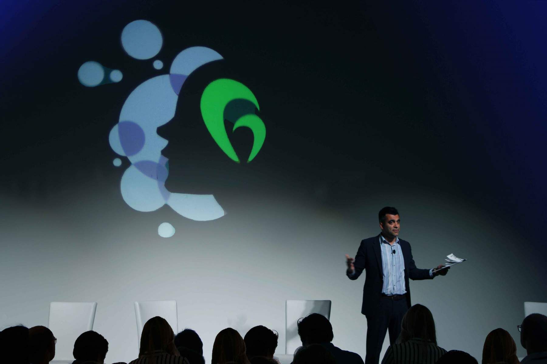 A man is standing on a stage giving a presentation to a group of people.