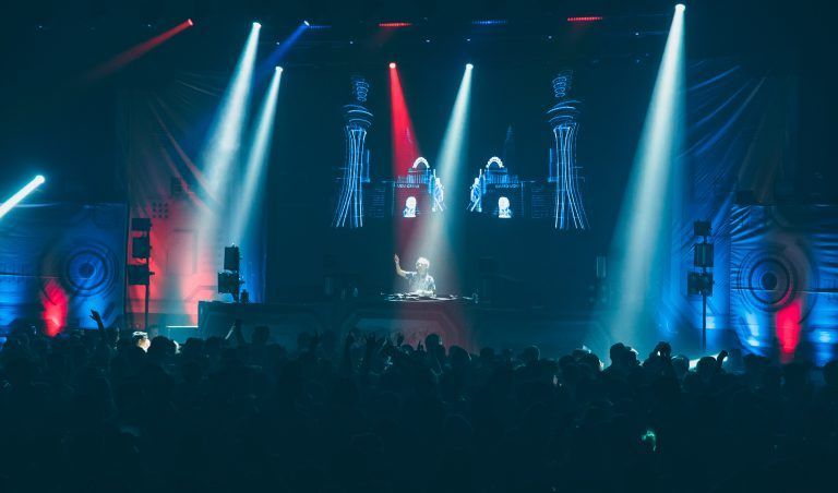A crowd of people are watching a dj on stage at a concert.