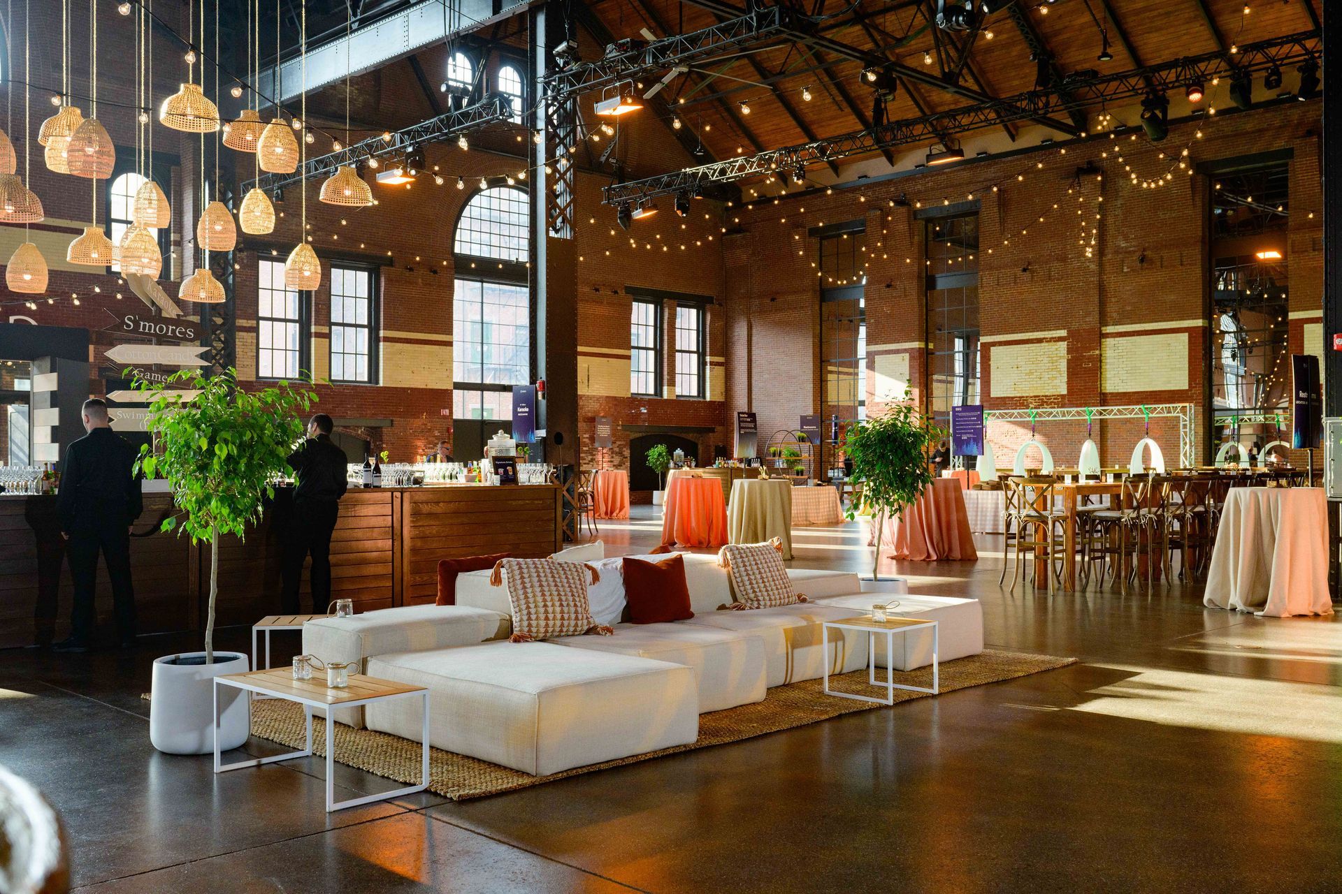 Event space with white sofas, tables, and buffet, warm lighting, brick walls.