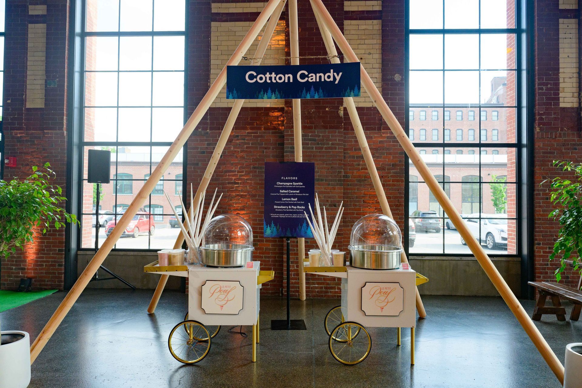 Two cotton candy machines under a wooden teepee, in a brick-walled room.