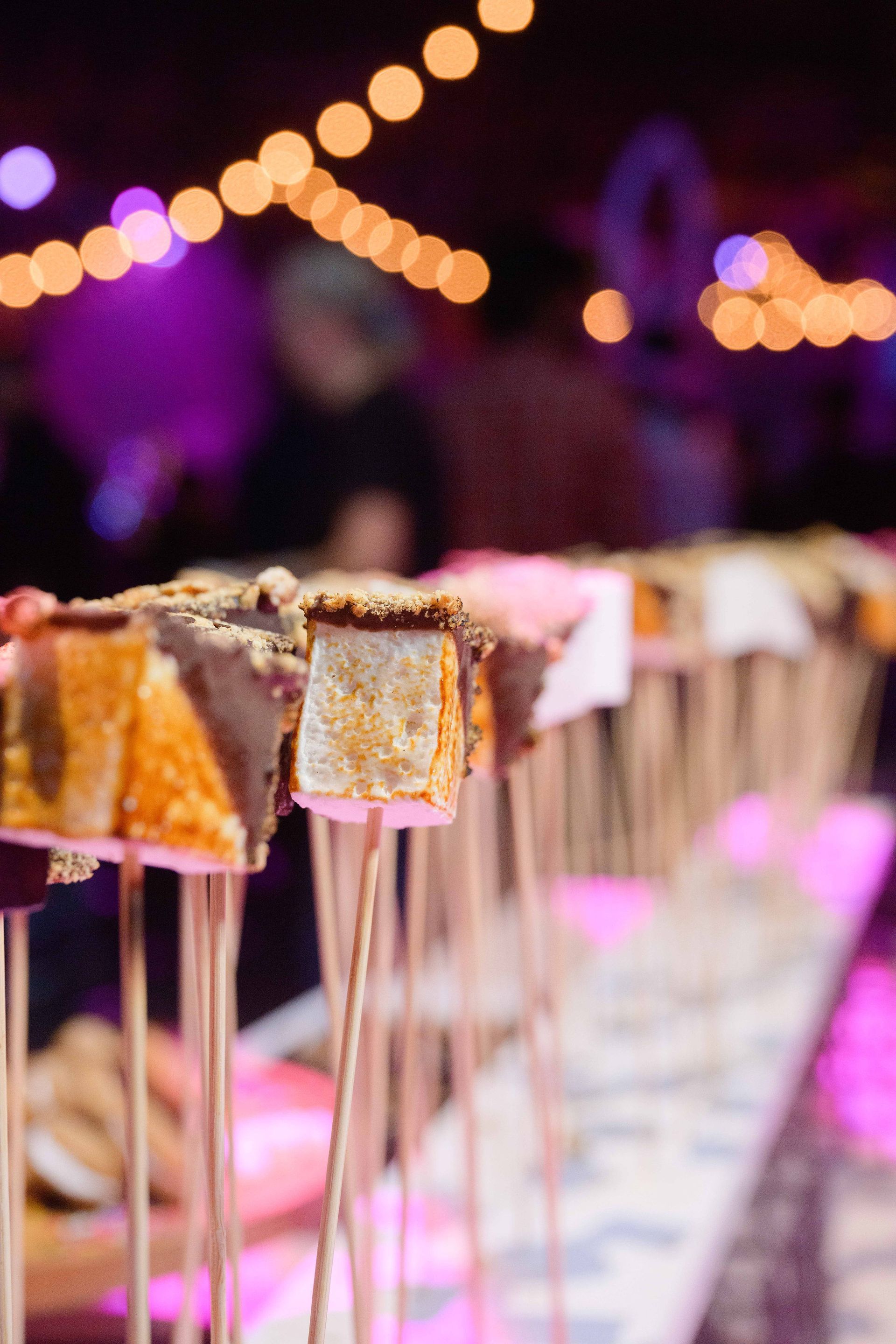 Marshmallow treats on skewers, displayed on a table under festive lights.