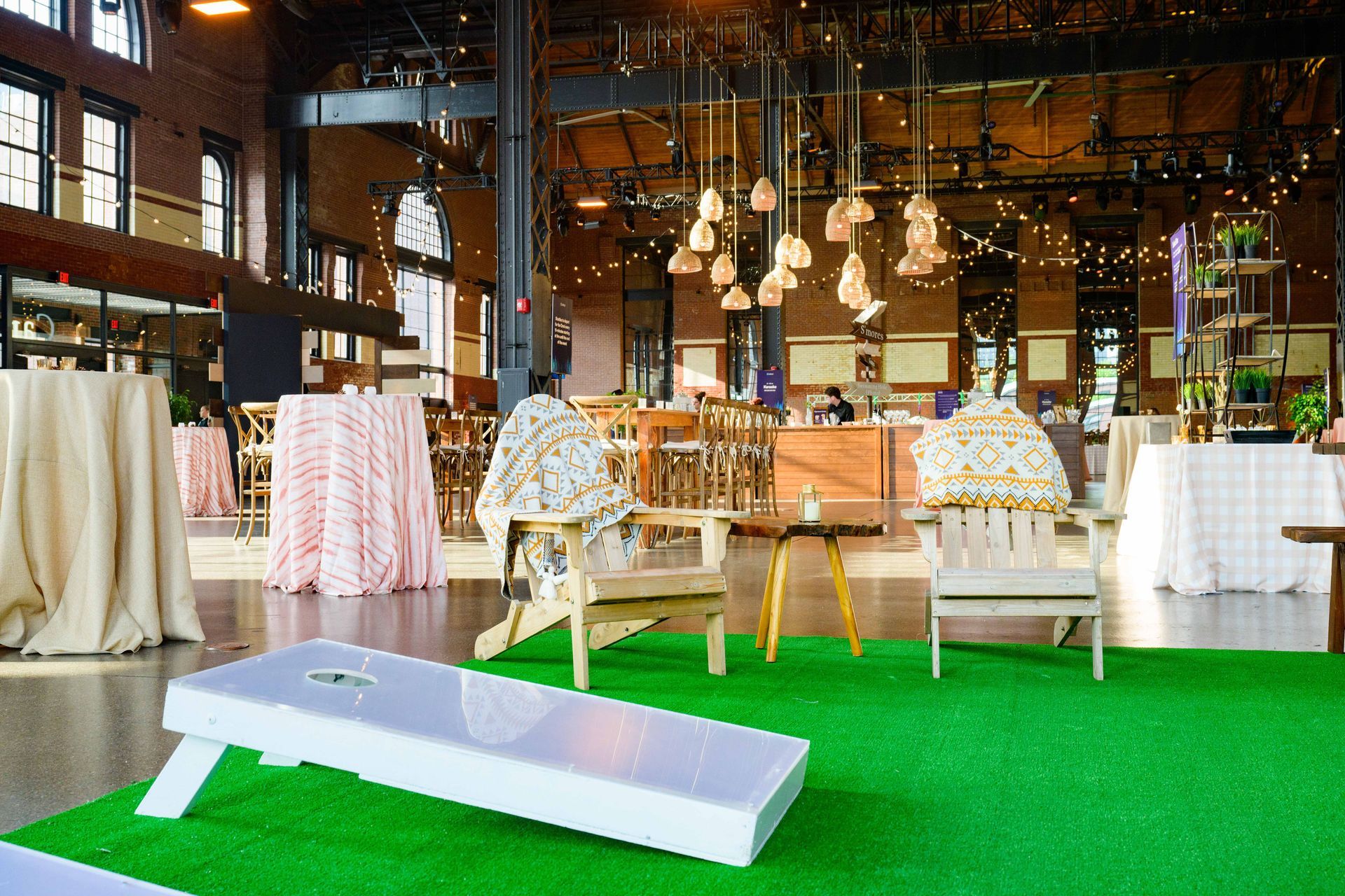 An event space with cornhole game set up on artificial turf, chairs, and tables.