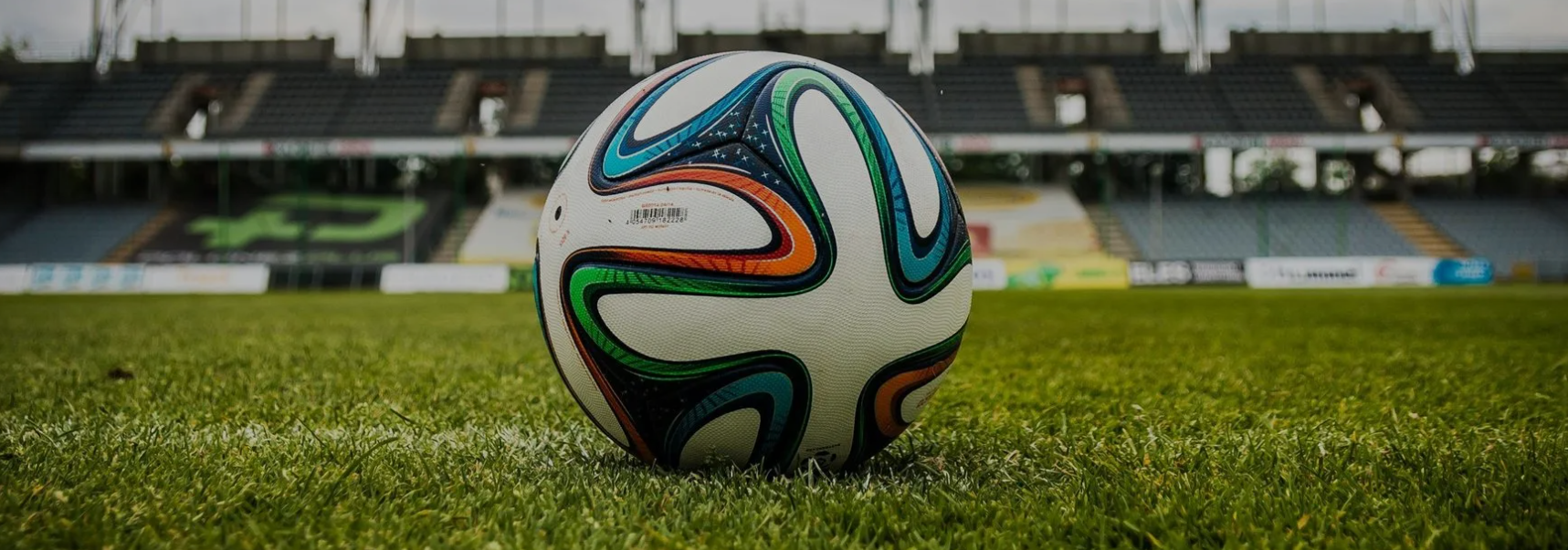 Soccer ball on a green field in front of an empty stadium seating.