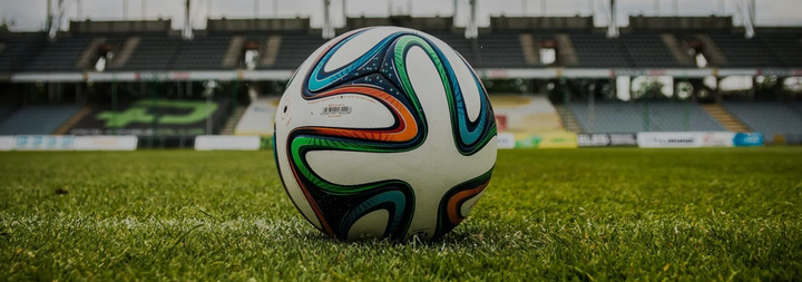 Soccer ball on a green field in front of an empty stadium seating.