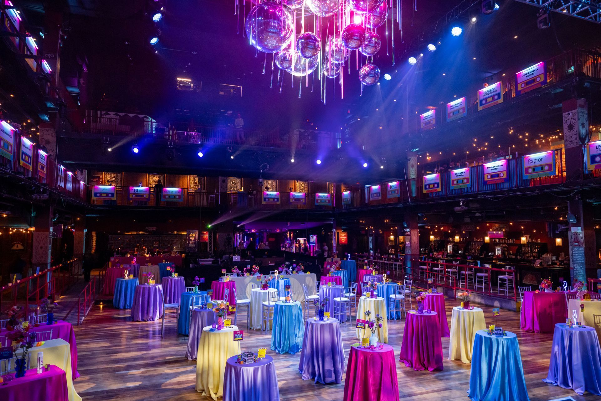 Event space with colorful tables, disco balls, and vibrant purple and blue lighting.