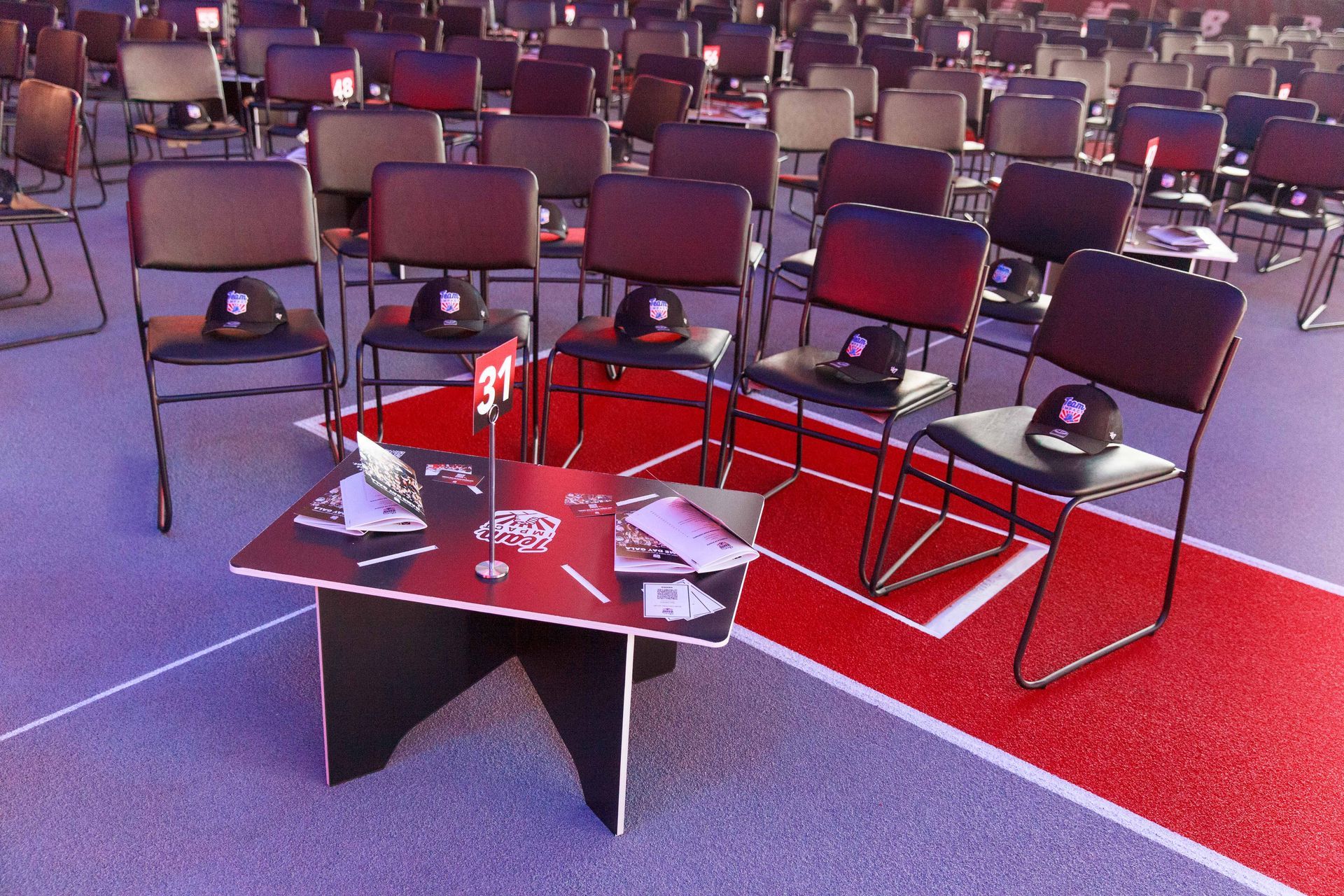 Rows of chairs in an auditorium; a table with hats and promotional materials on it. Red carpet.