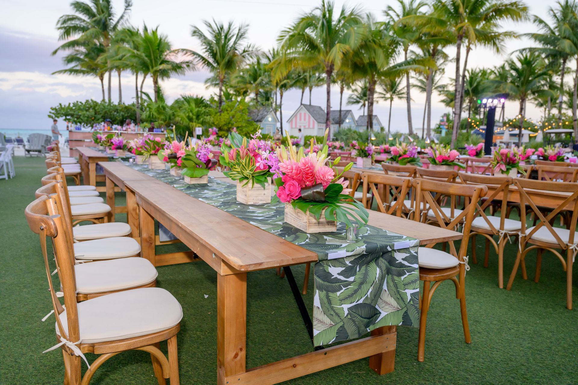 Outdoor event tables set with floral arrangements; palm trees in the background.