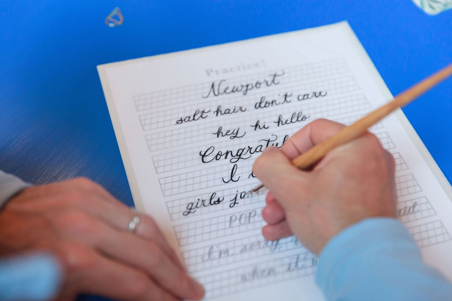 Person writing cursive with a pen on a practice sheet labeled 