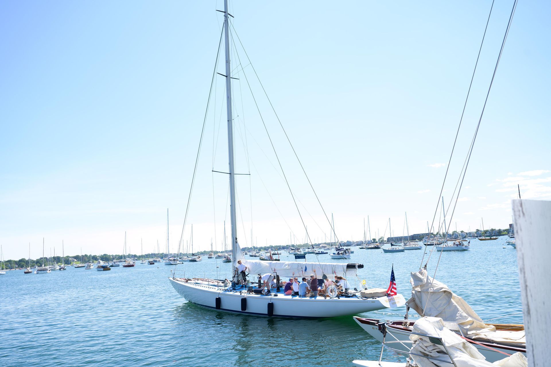 Sailboat on blue water, with passengers, under a clear blue sky. Many other boats in the background.