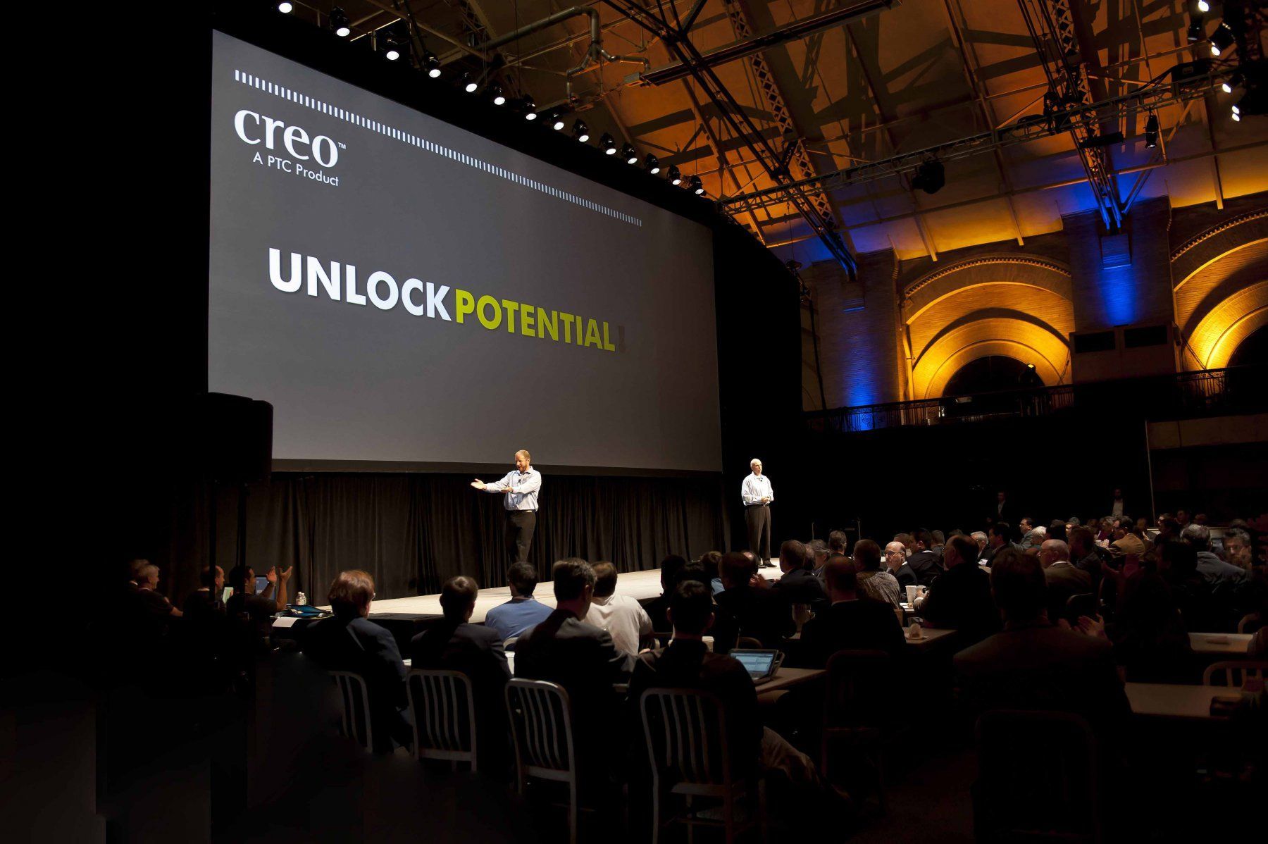 A man is giving a presentation in front of a large screen that says unlock potential.