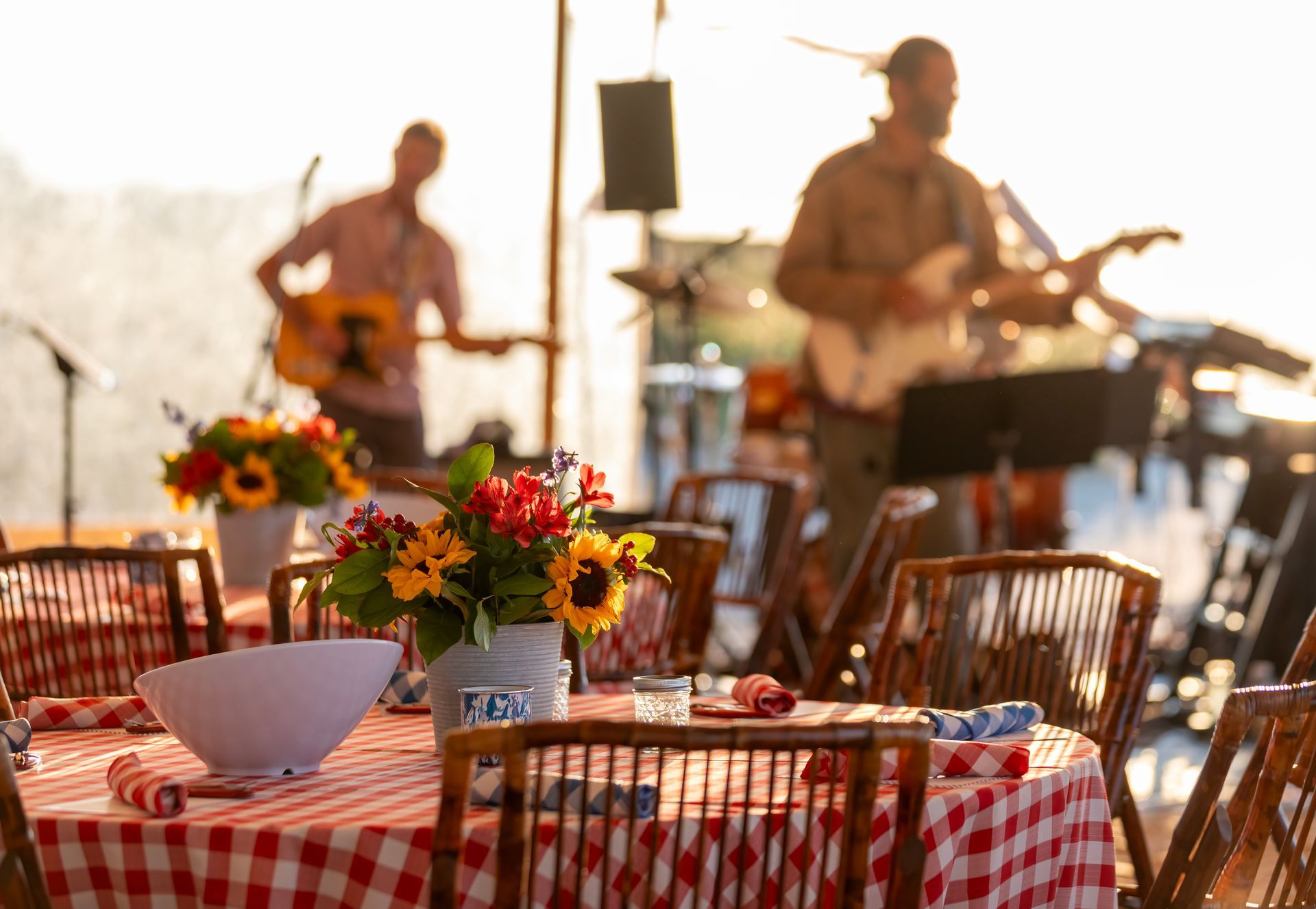 Tables set for outdoor dining with a band playing in the background, sunflowers in a vase.
