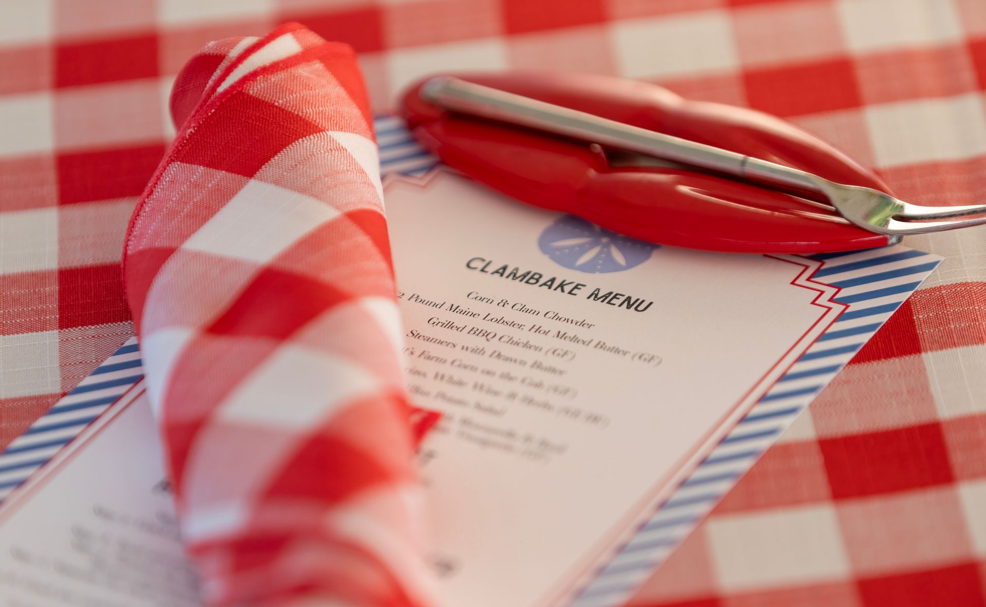 Red and white checkered tablecloth with folded napkin, menu, and lobster cracker.